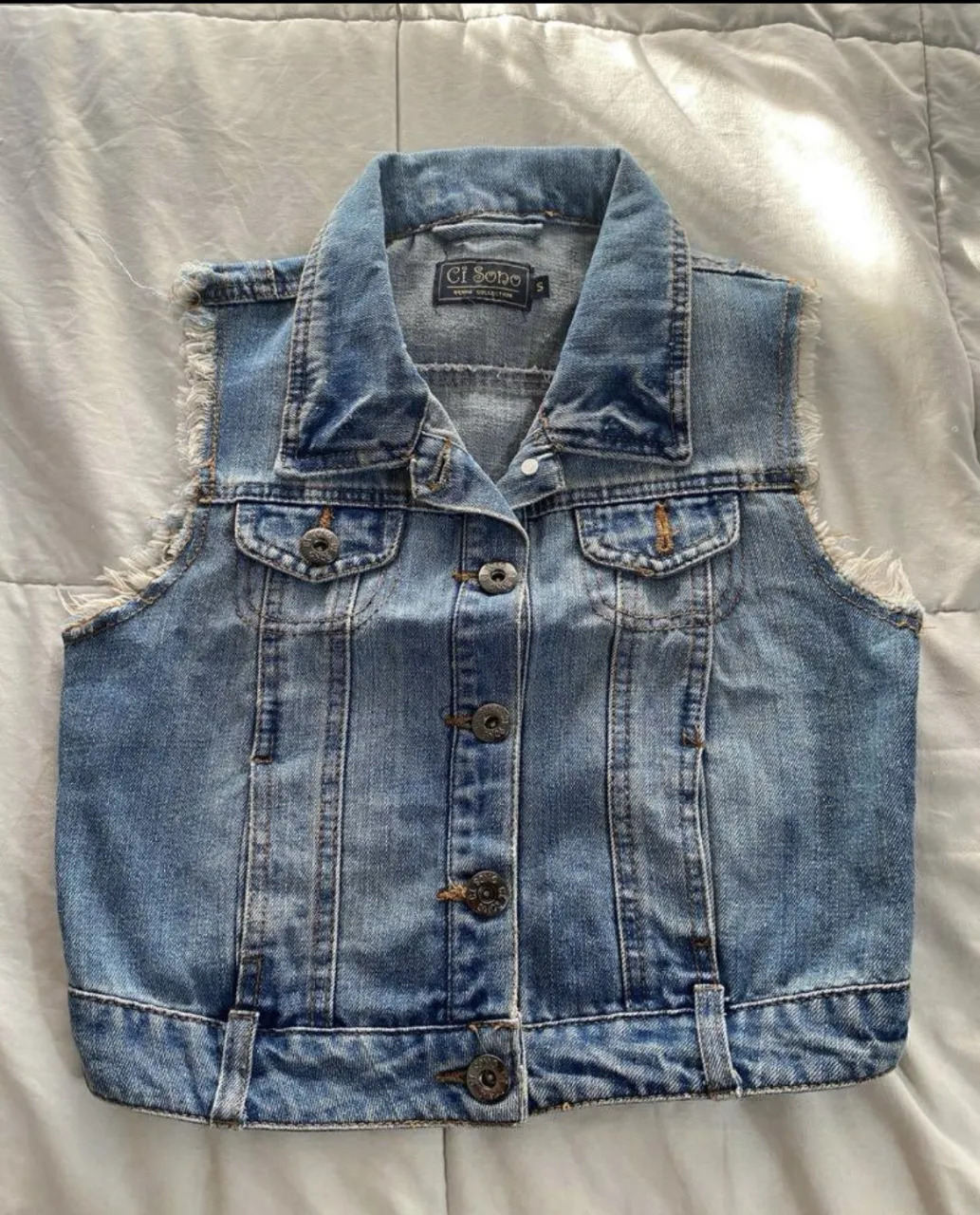 Chaleco de jean azul claro, con detalles deshilachados en los bordes. Tiene botones y bolsillos delanteros. Ideal para un look casual y moderno.