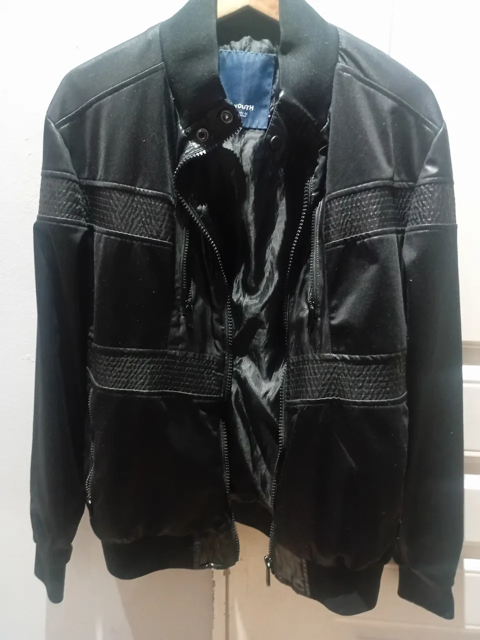 Campera bomber negra, con detalles texturizados en los paneles de mangas y torso. Cierre principal y bolsillos con cierre. Puños y cintura elastizados.
