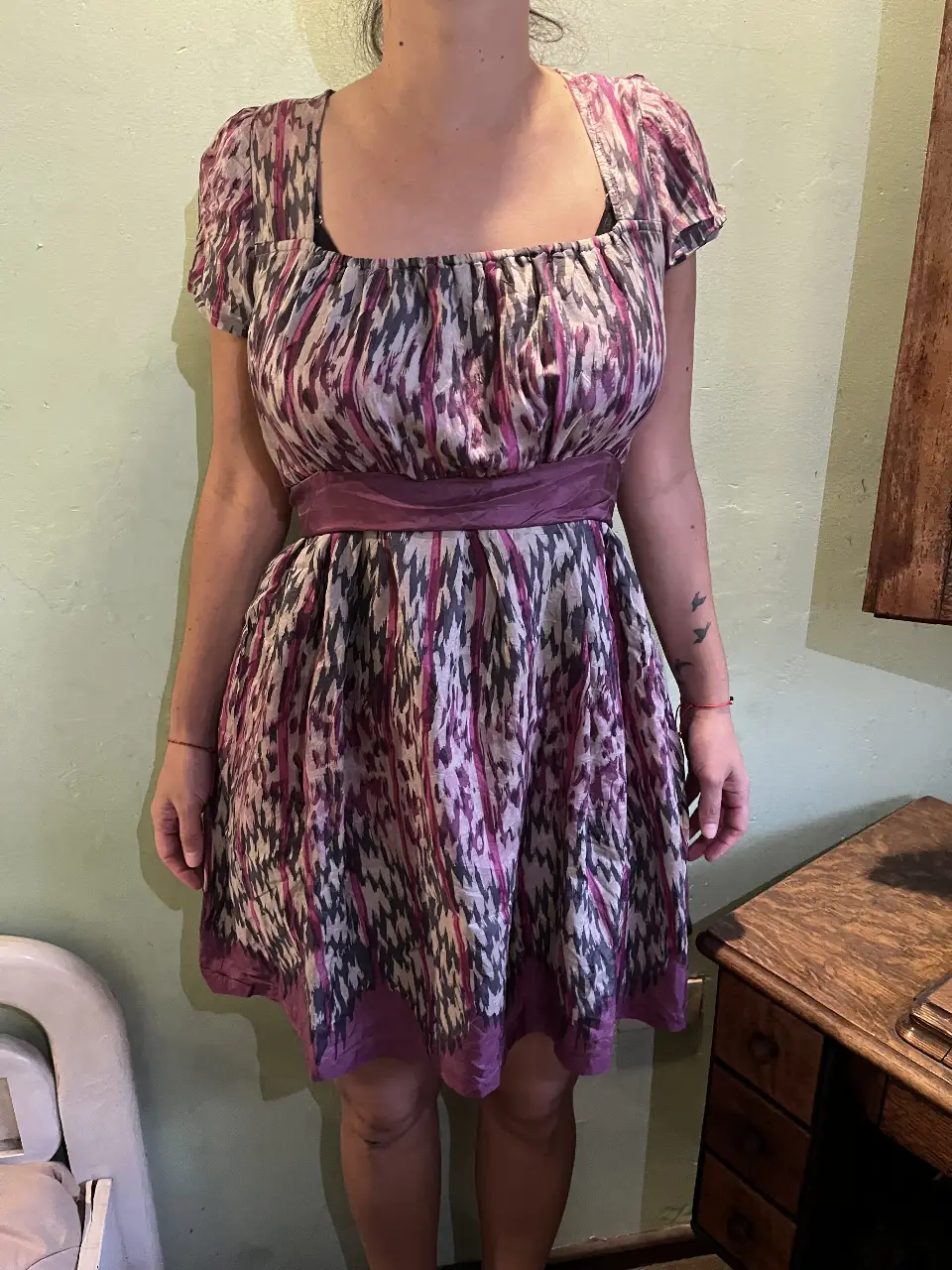 Vestido corto de mujer con estampado abstracto en tonos morados, grises y blancos. Cintura marcada con un cinturón a juego y escote cuadrado. Ideal para un look fresco y femenino.