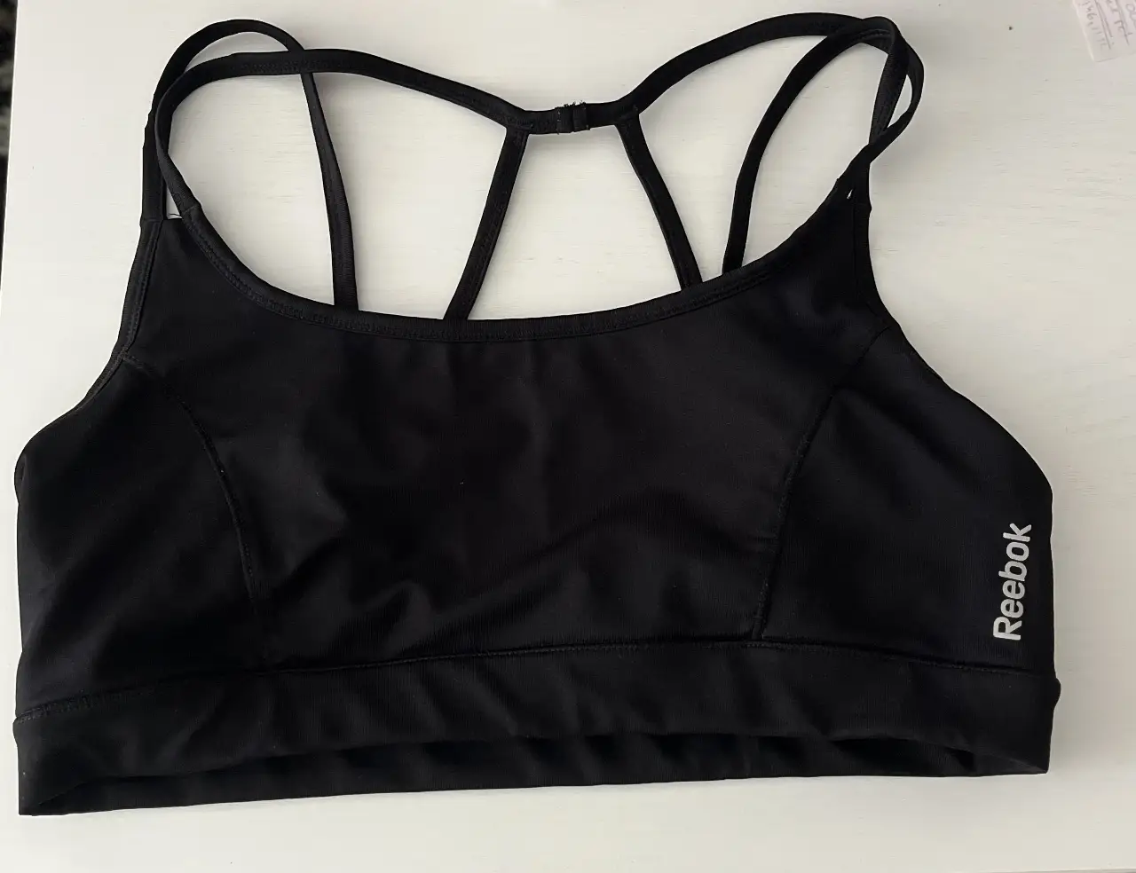 Top deportivo negro de la marca Reebok, ideal para actividades de alto impacto. Diseño con espalda cruzada y ajuste perfecto para mayor comodidad y soporte.