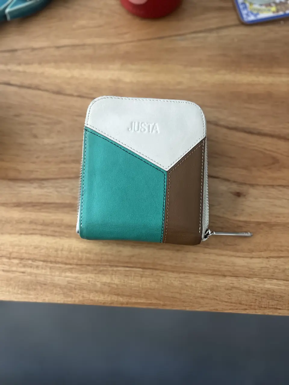 Billetera Justa de cuero, con diseño en bloques de color blanco, verde y marrón. Cierre perimetral y espacio para tarjetas.