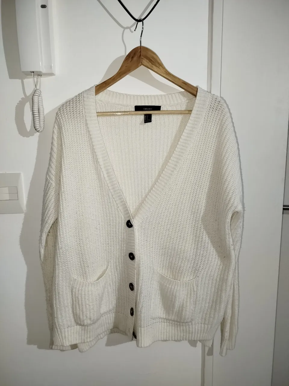 Cardigan tejido de punto grueso, color blanco, con botones y bolsillos delanteros. Ideal para un look casual y abrigado.