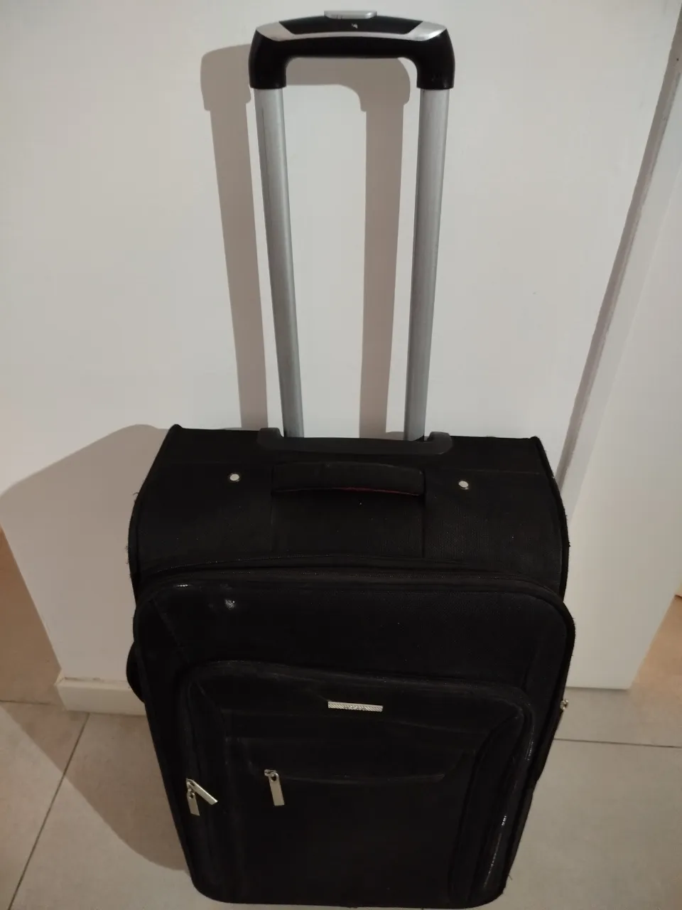 Valija de viaje negra, con manija extensible y ruedas. Ideal para viajes cortos o medianos. Cuenta con un bolsillo frontal y un compartimento principal amplio.