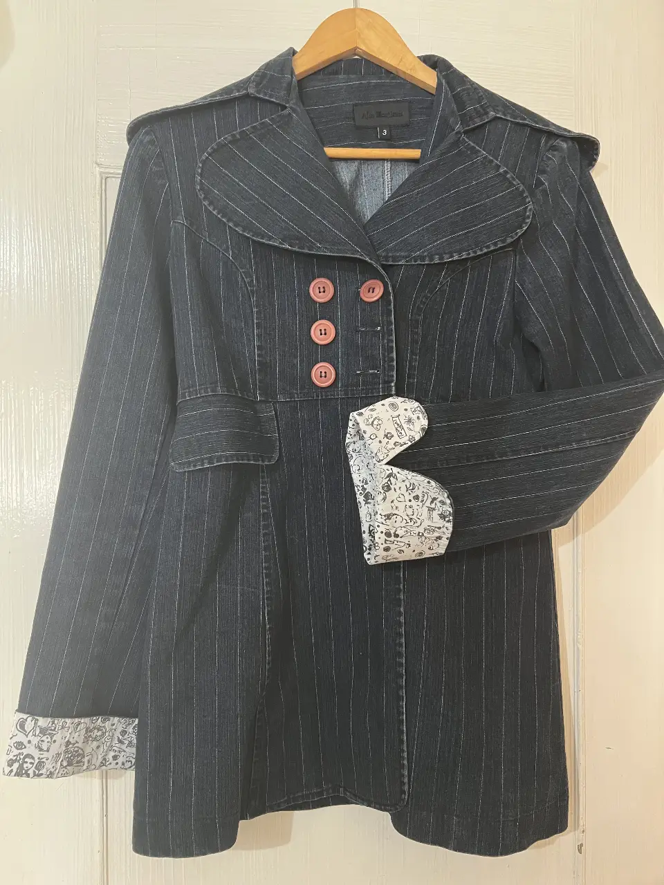 Sobretodo de jean negro con diseño de rayas verticales. Posee botones color rosa y detalles en las mangas con estampado. Marca Allo Martinez, talle 3.