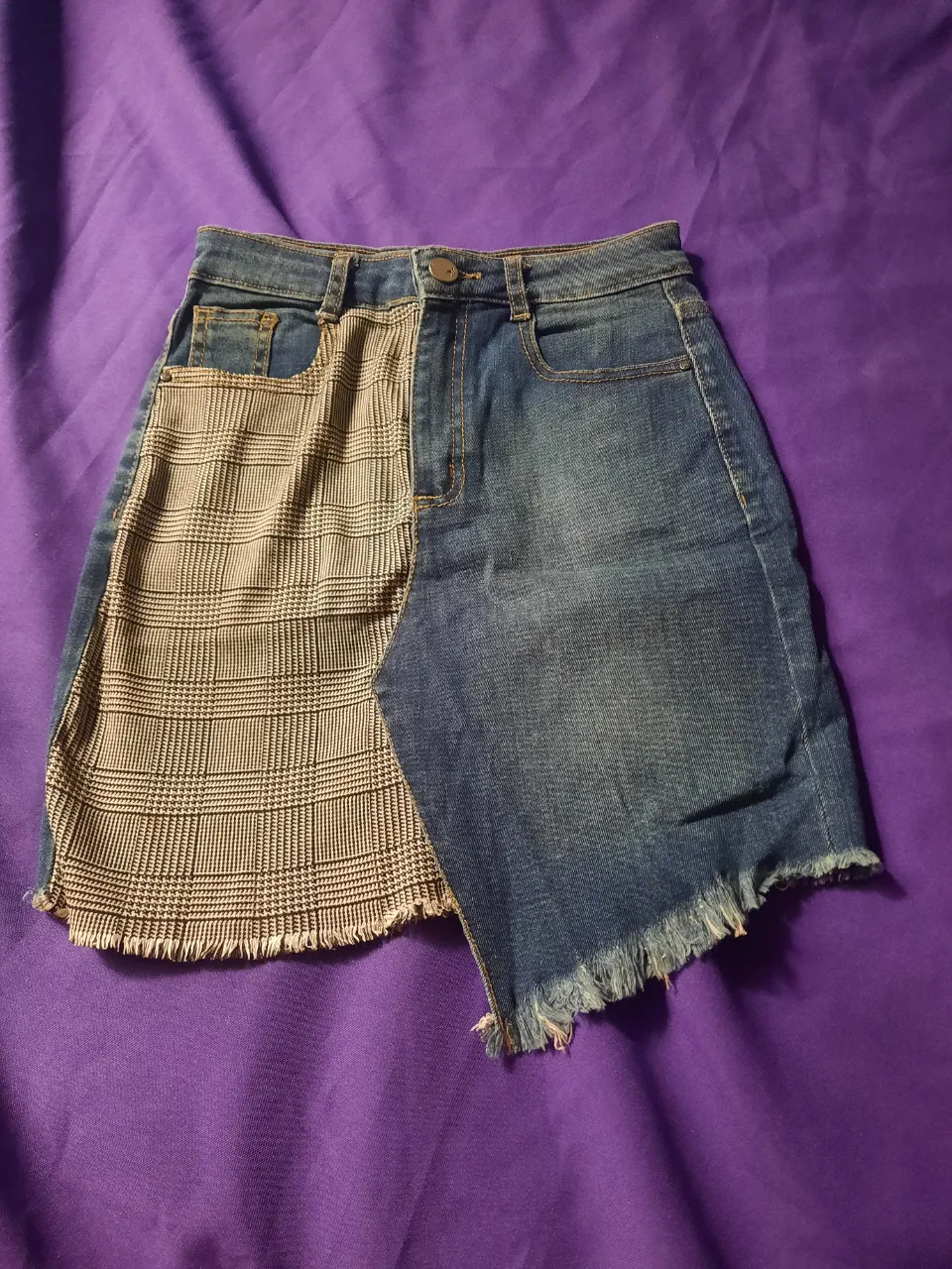 Pollera de jean intervenida con tela escocesa. Posee detalles desflecados en el borde inferior. Es elastizada