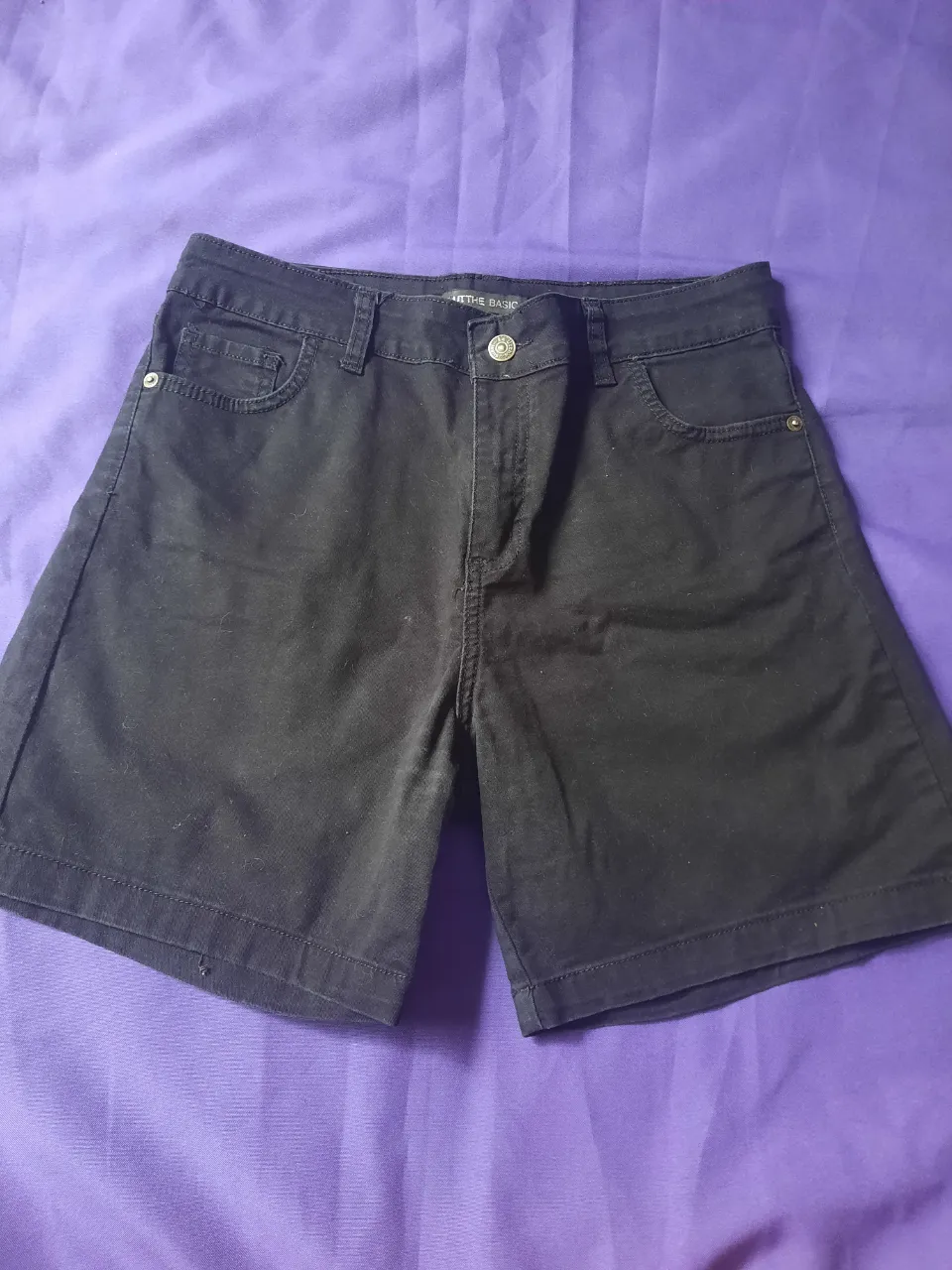 Shorts de jean negros, tipo bermuda ancha, con bolsillos delanteros y traseros. Cierre con botón.