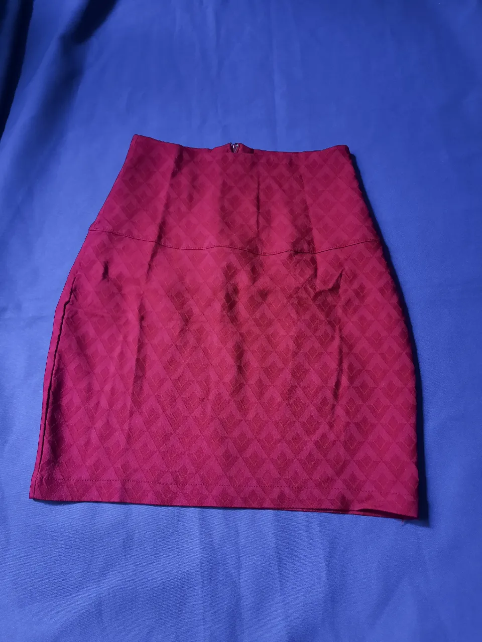 Pollera corta de color rojo intenso con un estampado de rombos en relieve. Posee cierre en la parte trasera.