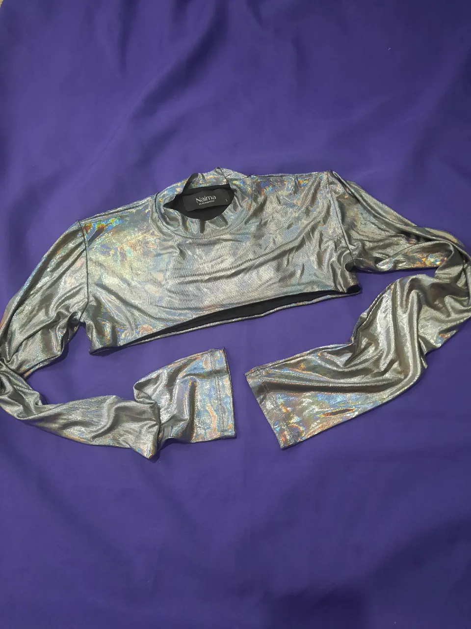 Top plateado metalizado con mangas largas y cuello redondo. La prenda es corta y las mangas son amplias.