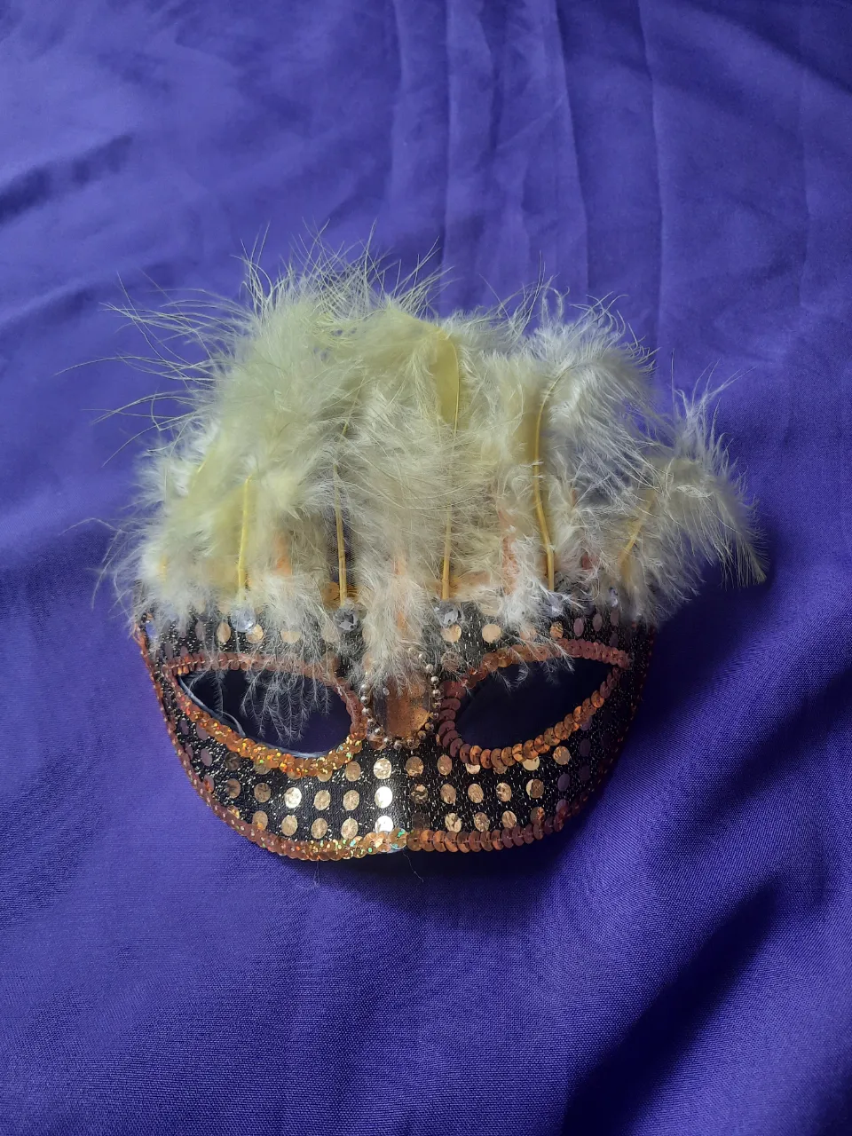 Máscara veneciana con lentejuelas doradas y negras, detalles de cuentas y plumas amarillas en la parte superior.