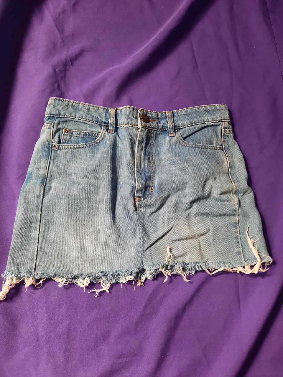 Pollera de jean corta con roturas y detalles deshilachados en el borde inferior. Presenta bolsillos delanteros y traseros. Talle S/M.