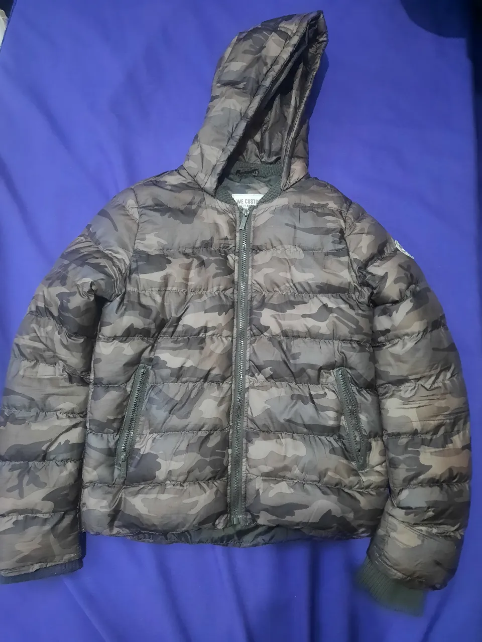 Campera acolchada con capucha y estampa de camuflaje. Posee cierre al frente y bolsillos laterales con cierre. Como nueva 

