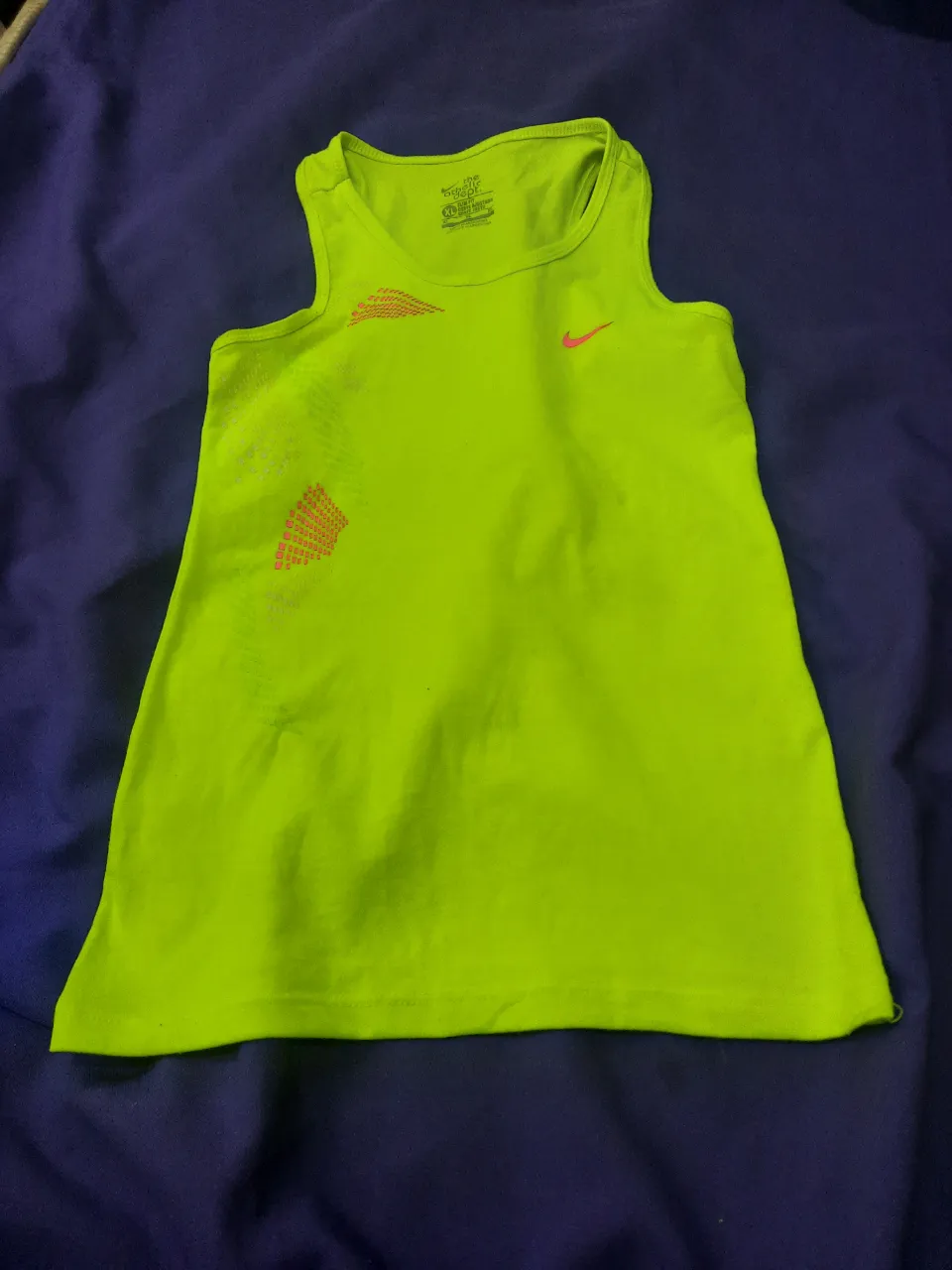 Musculosa deportiva de color verde flúor con estampa naranja y logo de Nike en el frente. Puede ceder hasta un M.