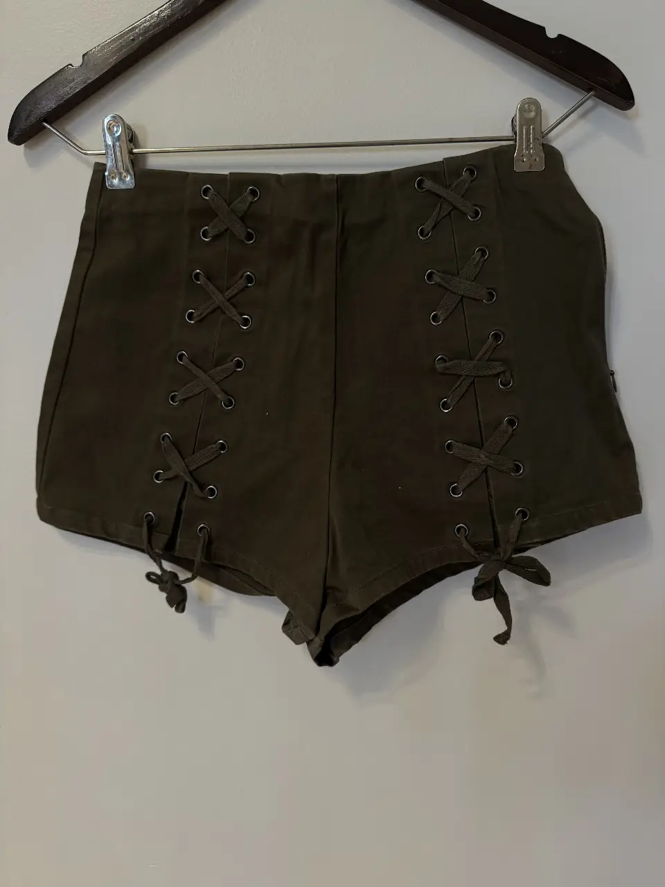 Short de tiro alto de color verde oscuro con detalles de cordones en los laterales y cierre en un costado. Ideal para un look moderno y audaz.