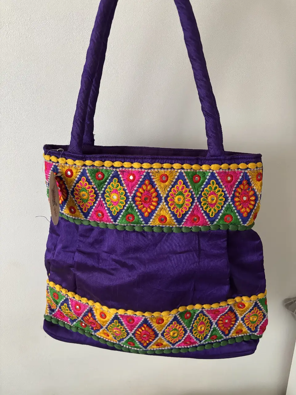 Bolso tote artesanal de tela morada con bordados coloridos y detalles de espejos. Traída de la India, aún con etiqueta. Es amplia, tiene un bolsillo interno. Entran cuadernos y cuenta con cierre para mayor seguridad. Muy boho