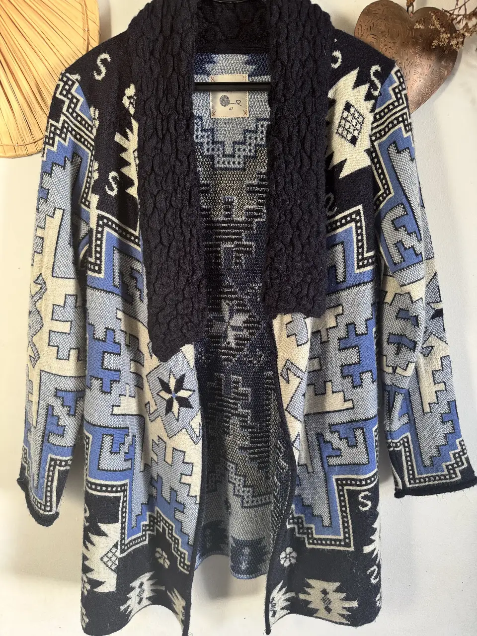 Cardigan tejido con diseño geométrico en tonos azul y blanco. Cuello con textura en color azul marino. Ideal para un look casual y abrigado.