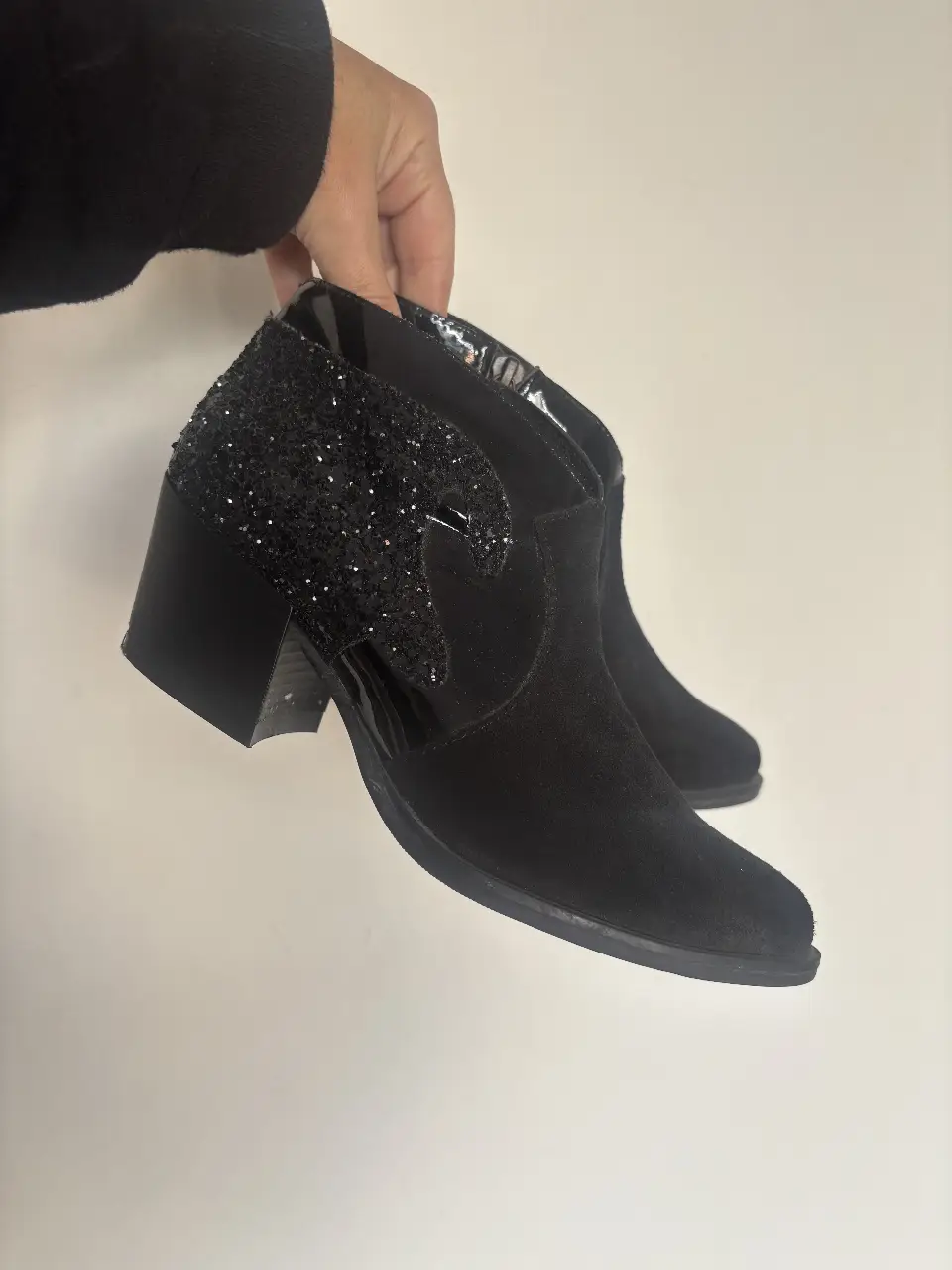 Botines negros de gamuza con detalles de glitter en el talón y un diseño de corte asimétrico. Ideales para darle un toque de glamour a tus looks de fiesta o salida.