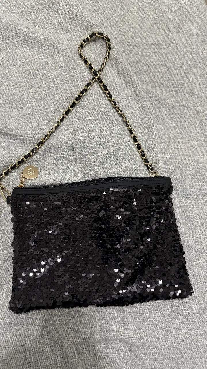 Cartera de mano negra con lentejuelas, ideal para fiestas y eventos especiales. Cuenta con una cadena dorada para llevar al hombro o cruzada. Un accesorio elegante y llamativo para completar tu look.