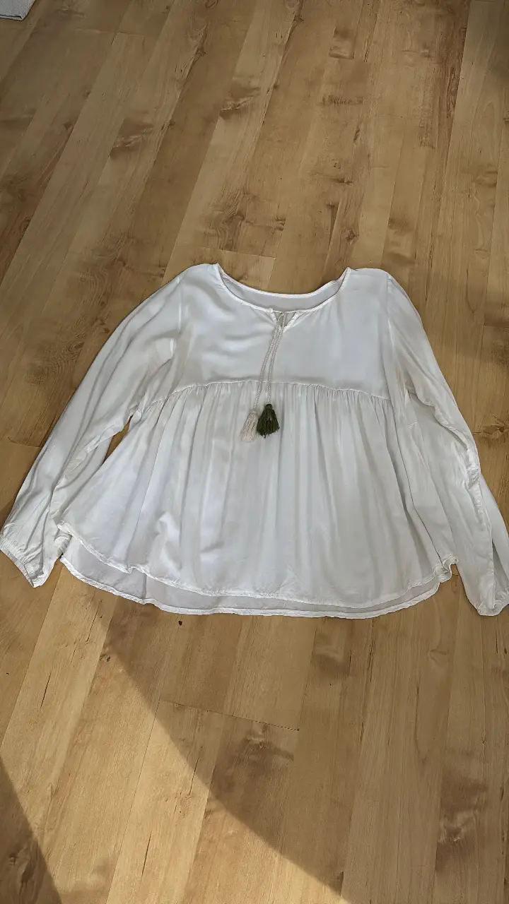Blusa blanca de manga larga con detalles de borlas en el cuello. Ideal para un look casual y fresco.