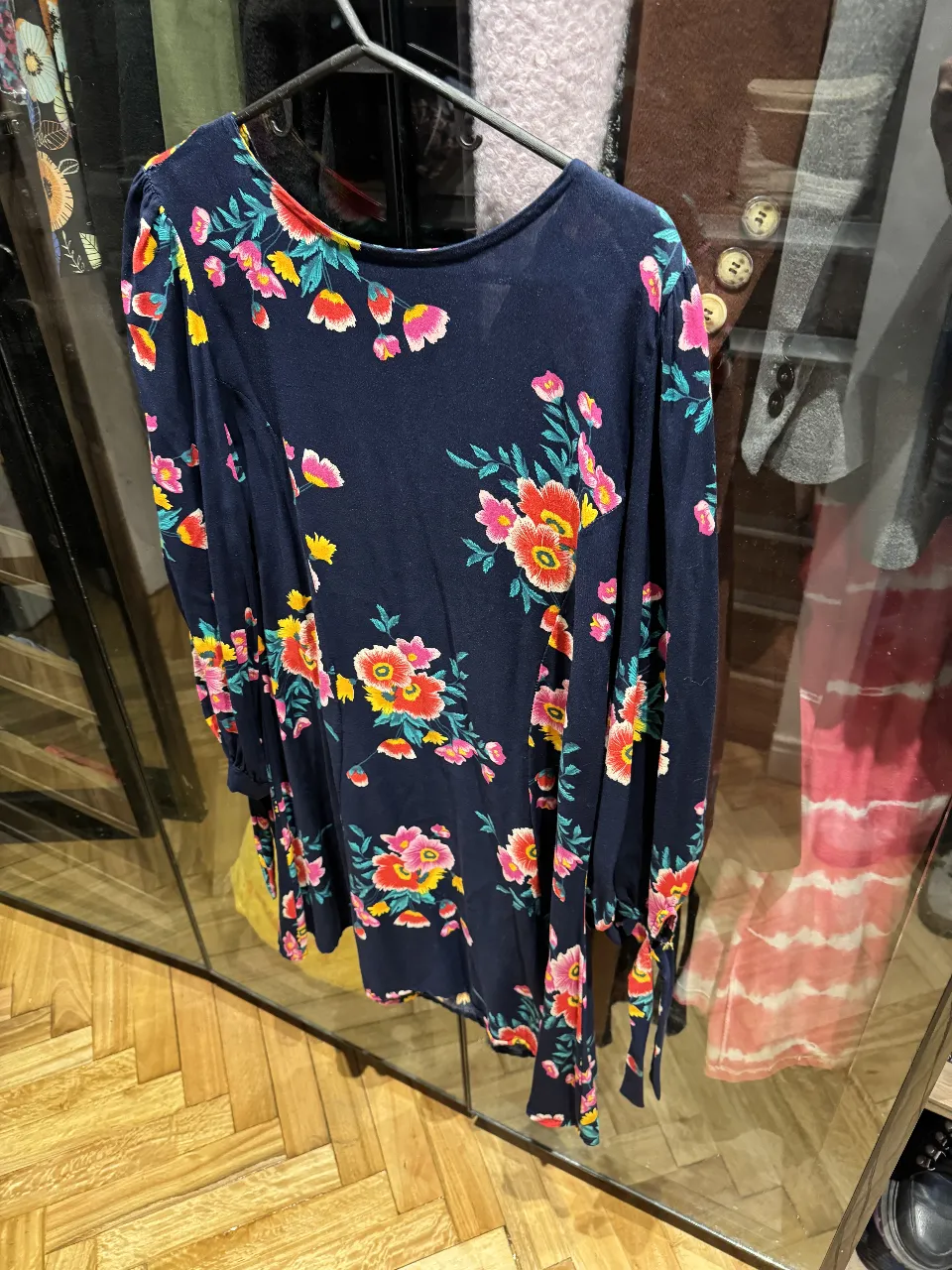 camisola o vestido midi de mujer con estampado floral en tonos rosa, amarillo y rojo sobre fondo azul marino. Manga larga con detalle de lazo en los puños. Ideal para un look casual y femenino.
