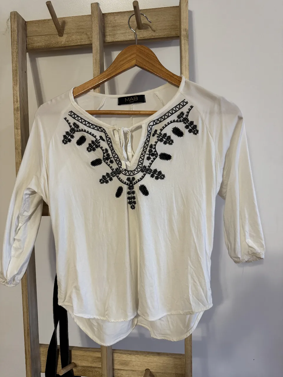 Blusa blanca con bordado negro en el escote y mangas 3/4. Ideal para un look casual y fresco.
