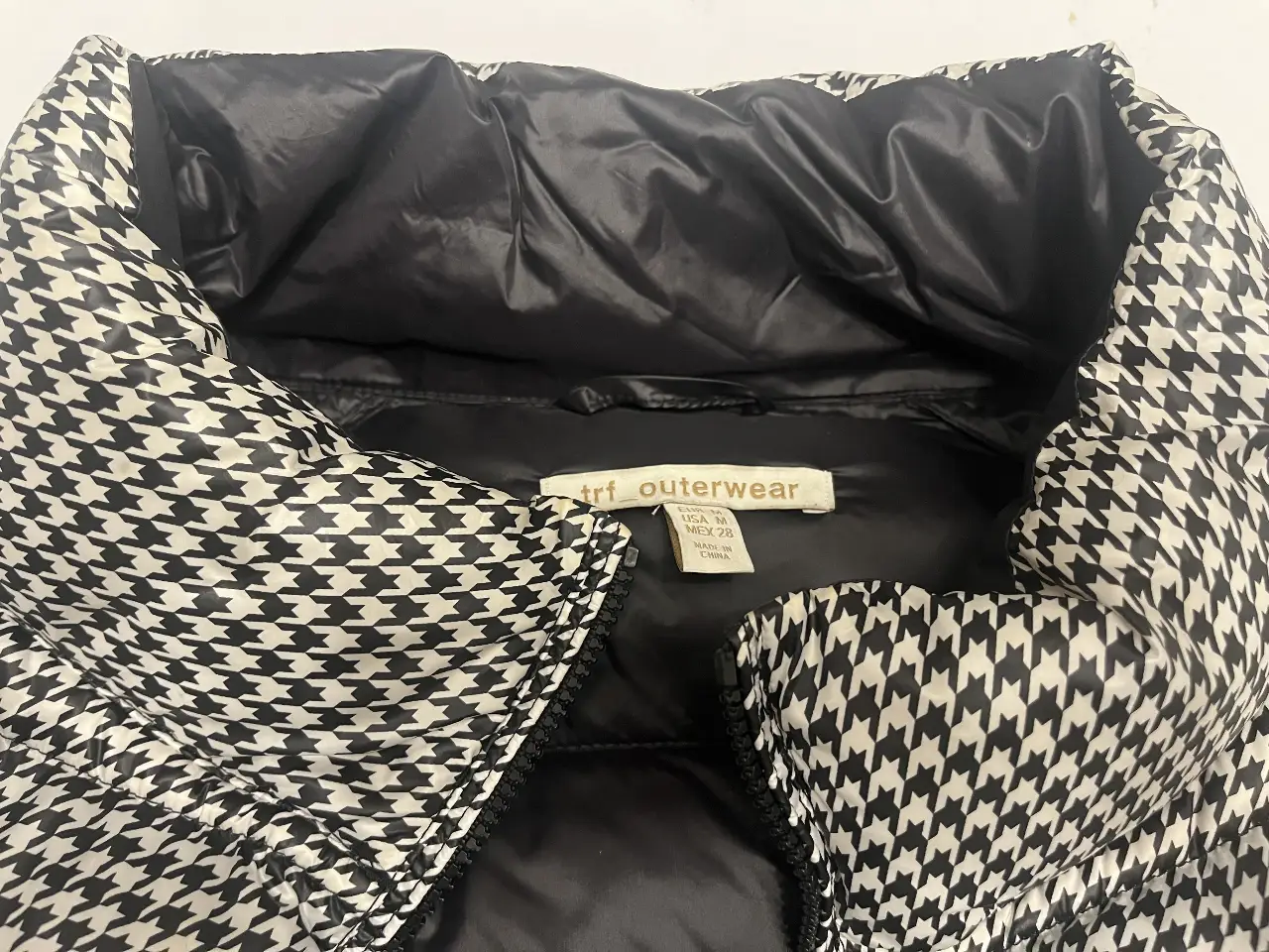 Campera de pluma con estampado de pata de gallo en blanco y negro. Ideal para el invierno, con cuello alto y cierre frontal. Marca trf_outerwear.