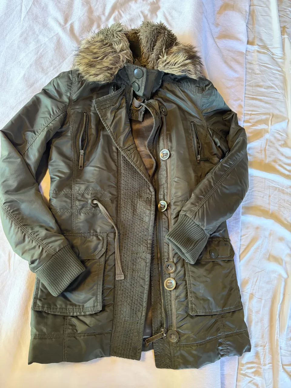 Campera de abrigo con cuello de piel sintética, ideal para el frío. Posee múltiples bolsillos con cierre y botones, y cordón ajustable en la cintura para un calce perfecto. Su diseño moderno la hace ideal para cualquier ocasión.