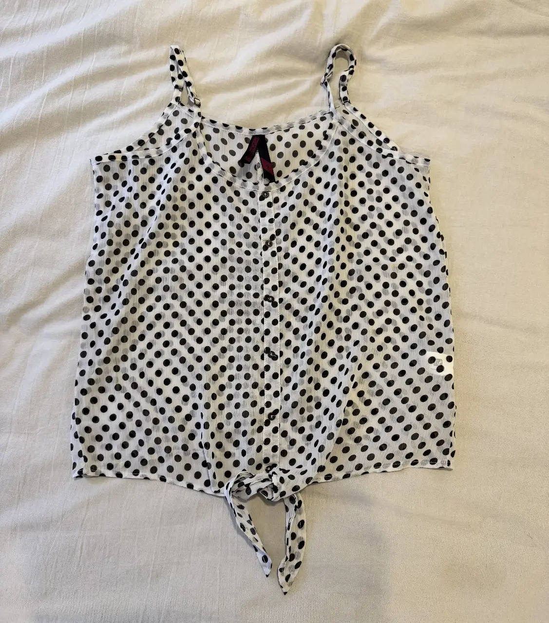 Musculosa con estampado de lunares en blanco y negro, con tirantes finos y detalle de lazo en la parte inferior. Ideal para un look casual y fresco.
