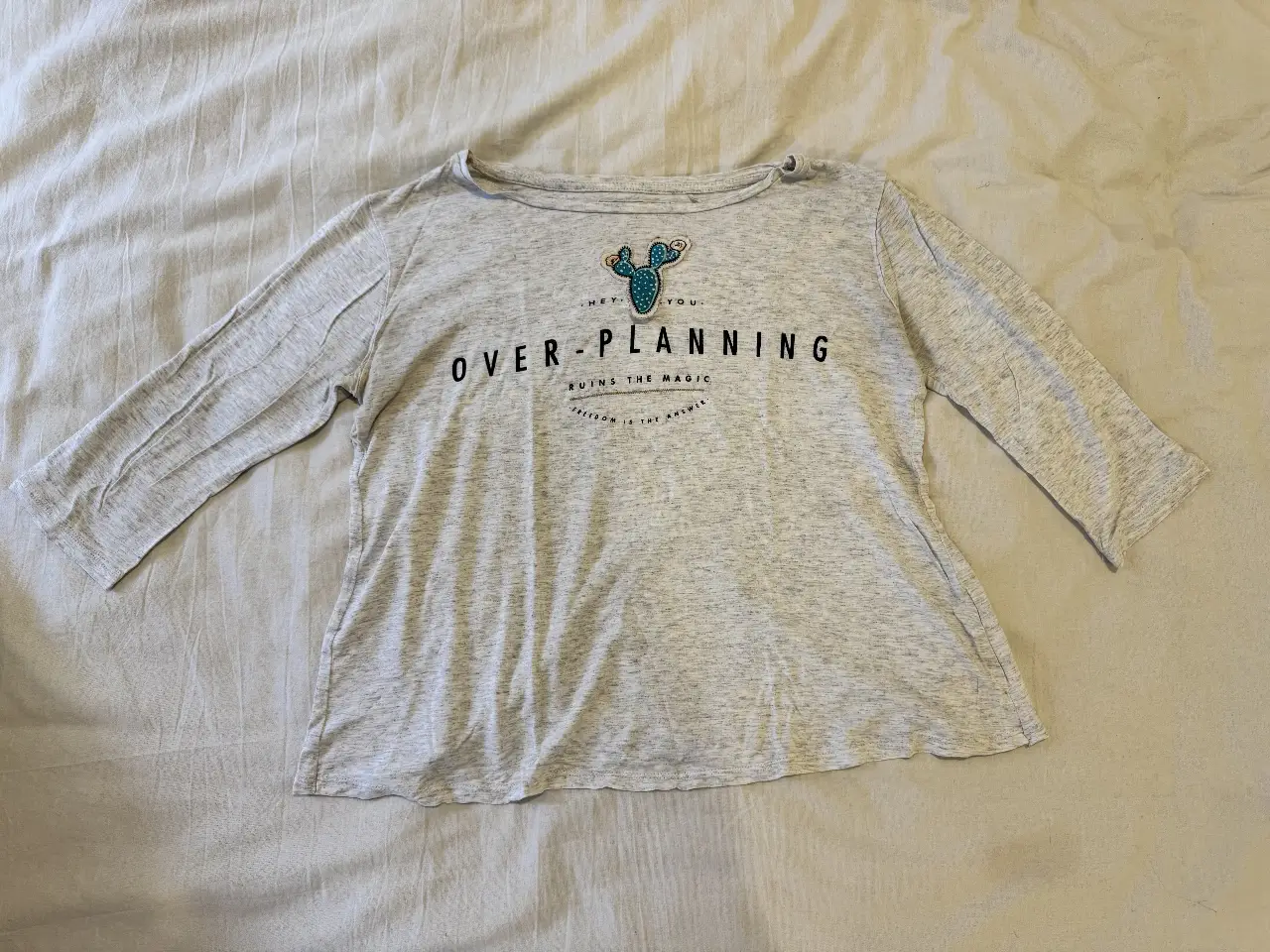 Remera manga tres cuartos gris con estampado de cactus y la frase "OVER-PLANNING RUINS THE MAGIC FREEDOM IS THE ANSWER". Ideal para un look casual y cómodo.