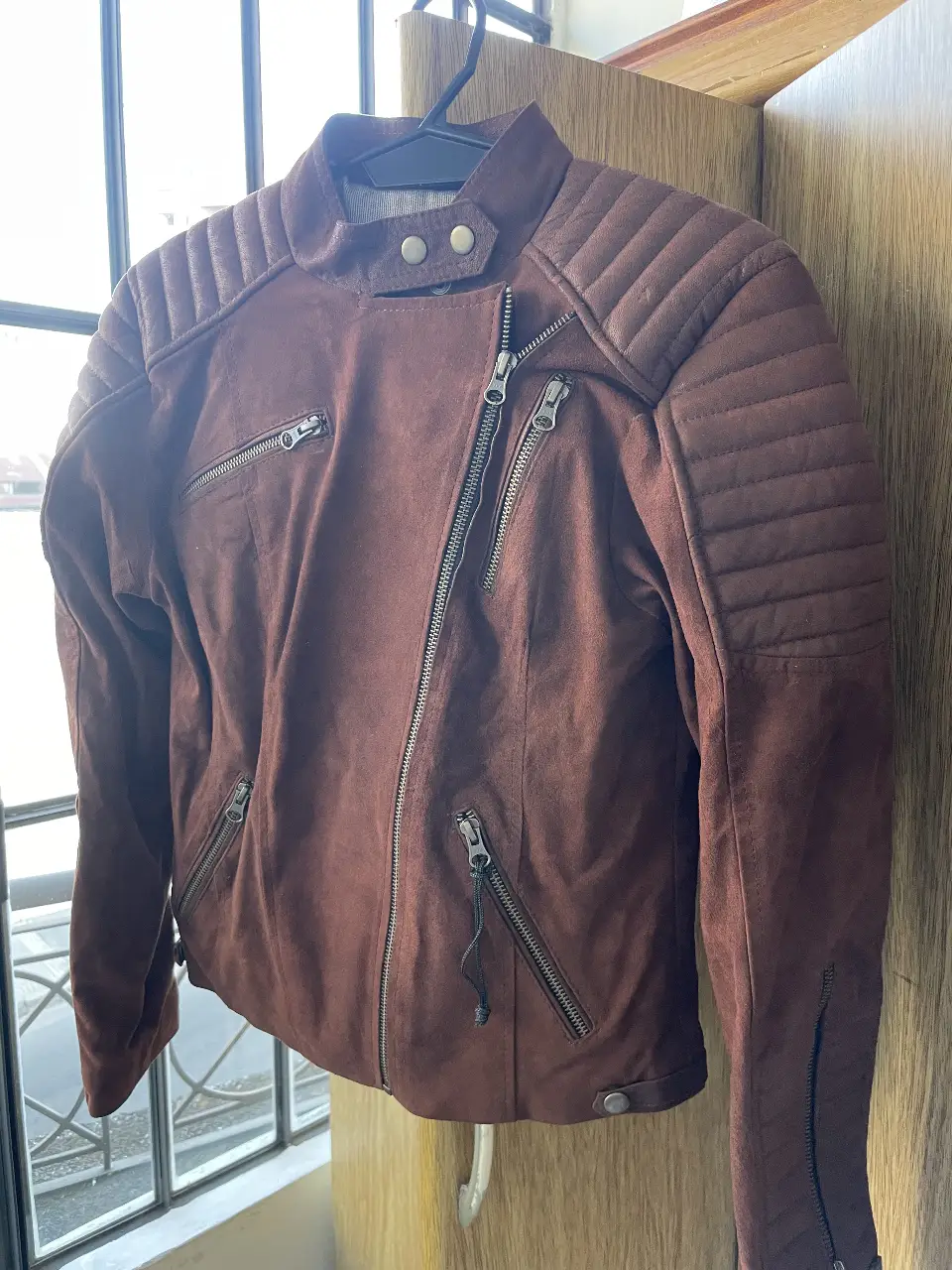 Campera unisex estilo biker en gamuza y cuero de cabra, color marrón. Detalles acolchados en hombros y mangas, cierre asimétrico y múltiples bolsillos con cierres. Marca Bs. As. - Argentina.
