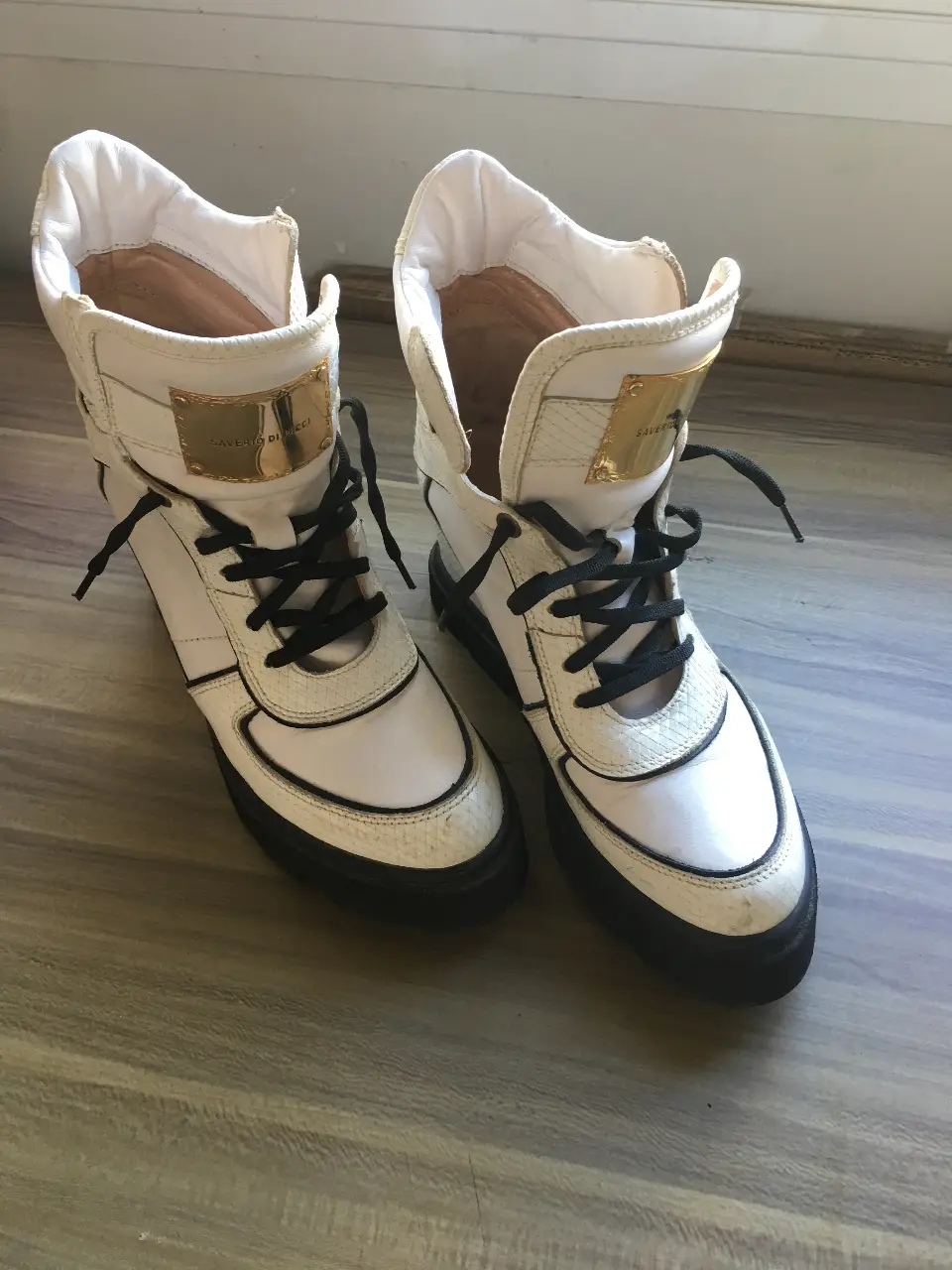Botas de caña alta blancas con detalles en negro y apliques dorados. Diseño moderno y elegante, ideales para un look urbano y sofisticado. Perfectas para destacar en cualquier ocasión.