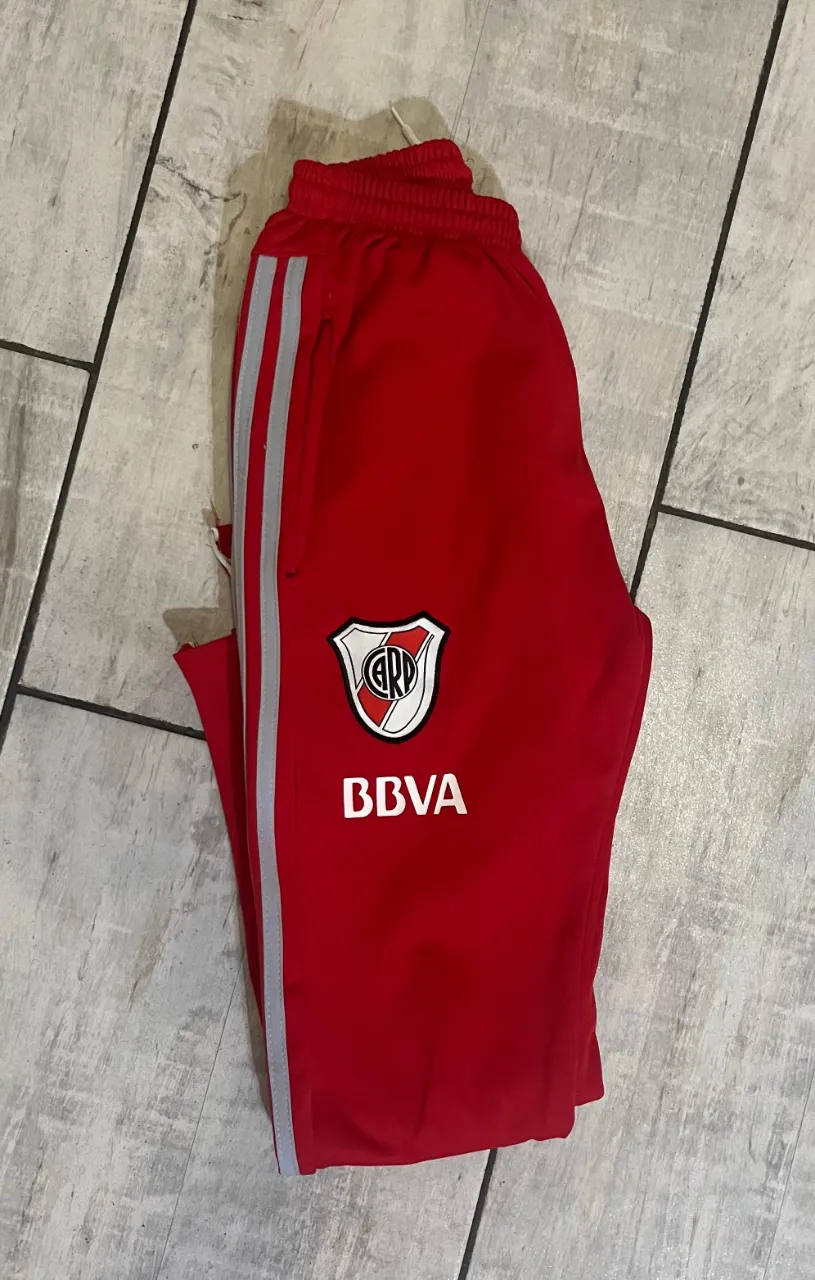 Pantalon deportivo de River Plate, color rojo, con detalles de Adidas y escudo del club. Ideal para fanáticos del fútbol.