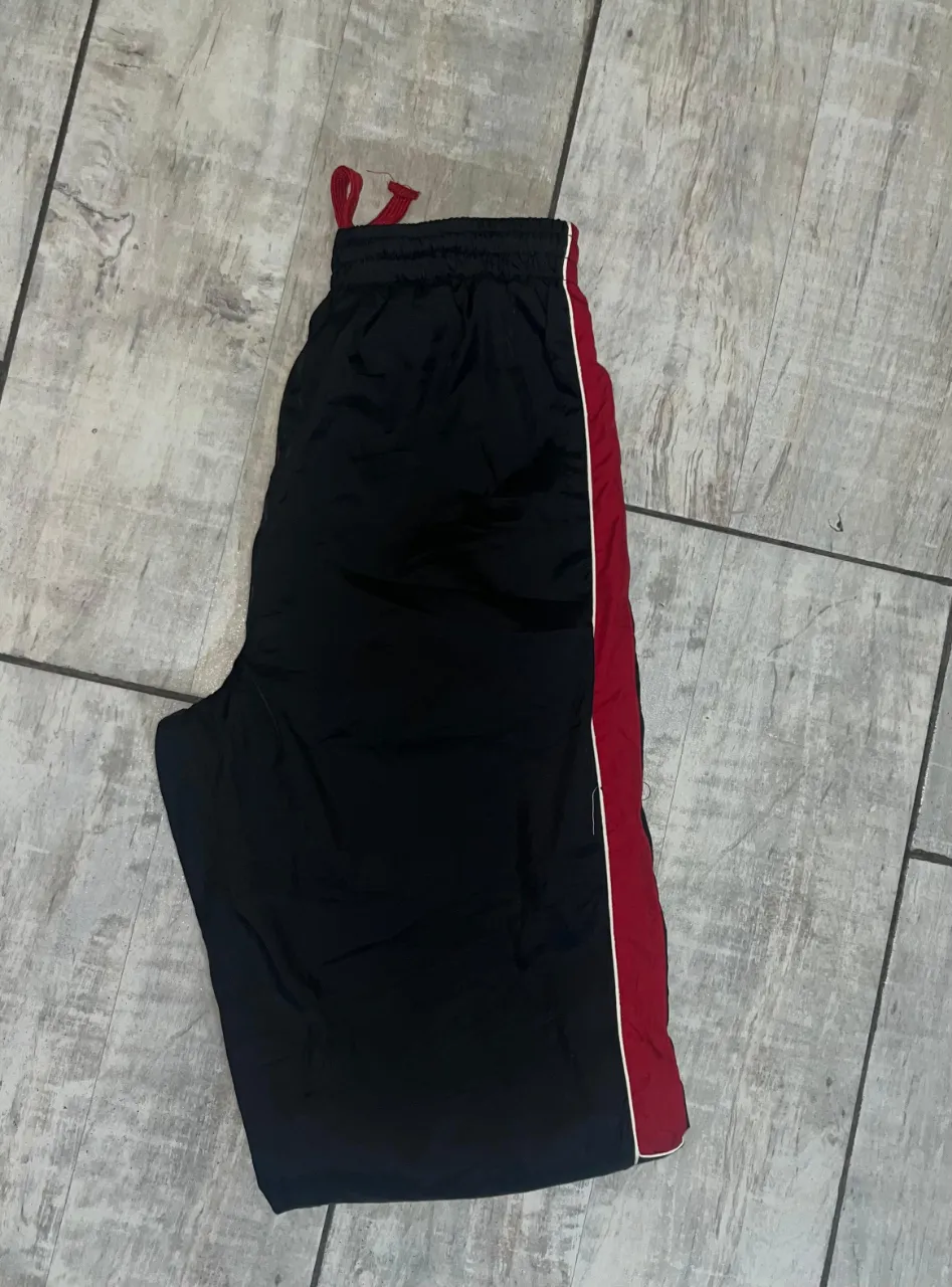 Pantalón deportivo negro con detalles en rojo y blanco. Ideal para entrenar o para un look urbano. tipo vintage, rompe vientos 
