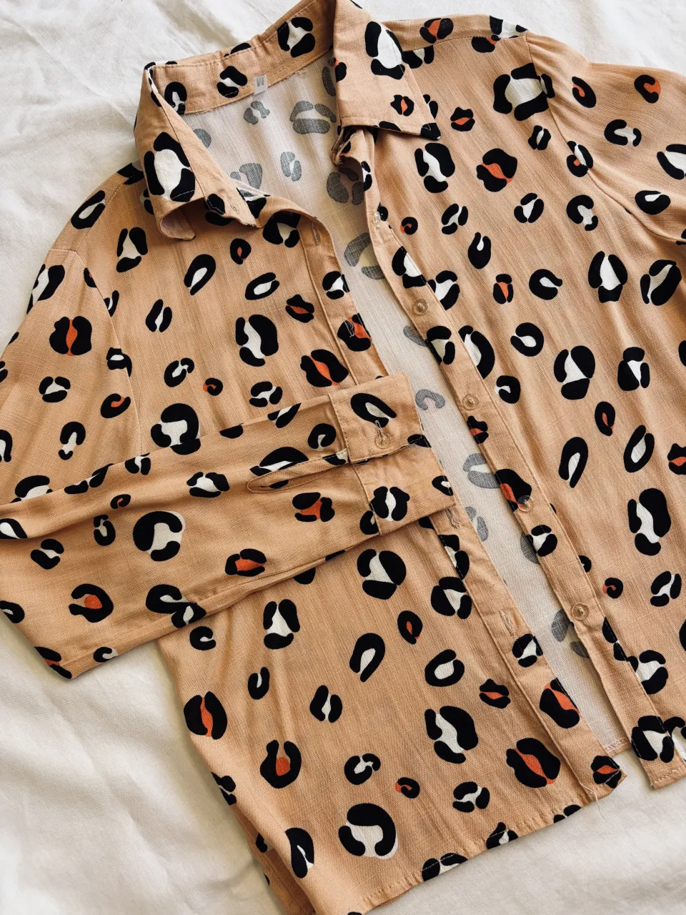 Camisa de manga larga con estampa de leopardo en tonos beige, negro, blanco y naranja. Posee cuello de camisa y botones al frente.