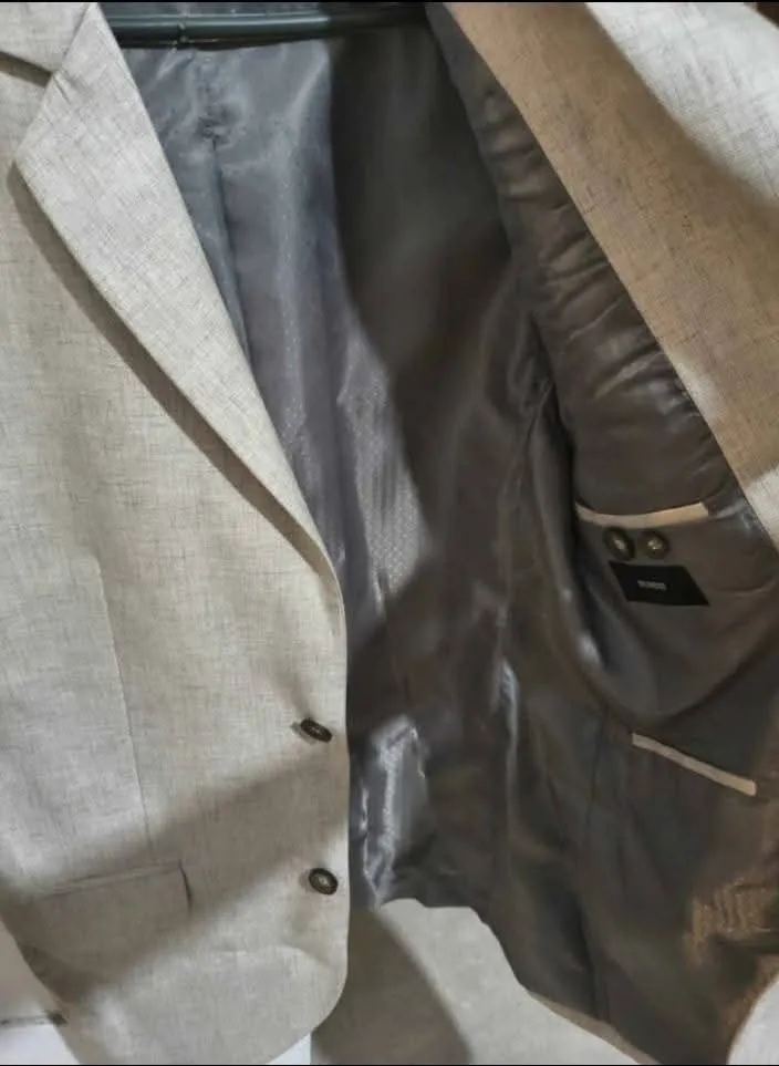 Saco de vestir color gris claro con dos botones al frente. Posee forro interior gris con un patrón de pequeños puntos blancos.