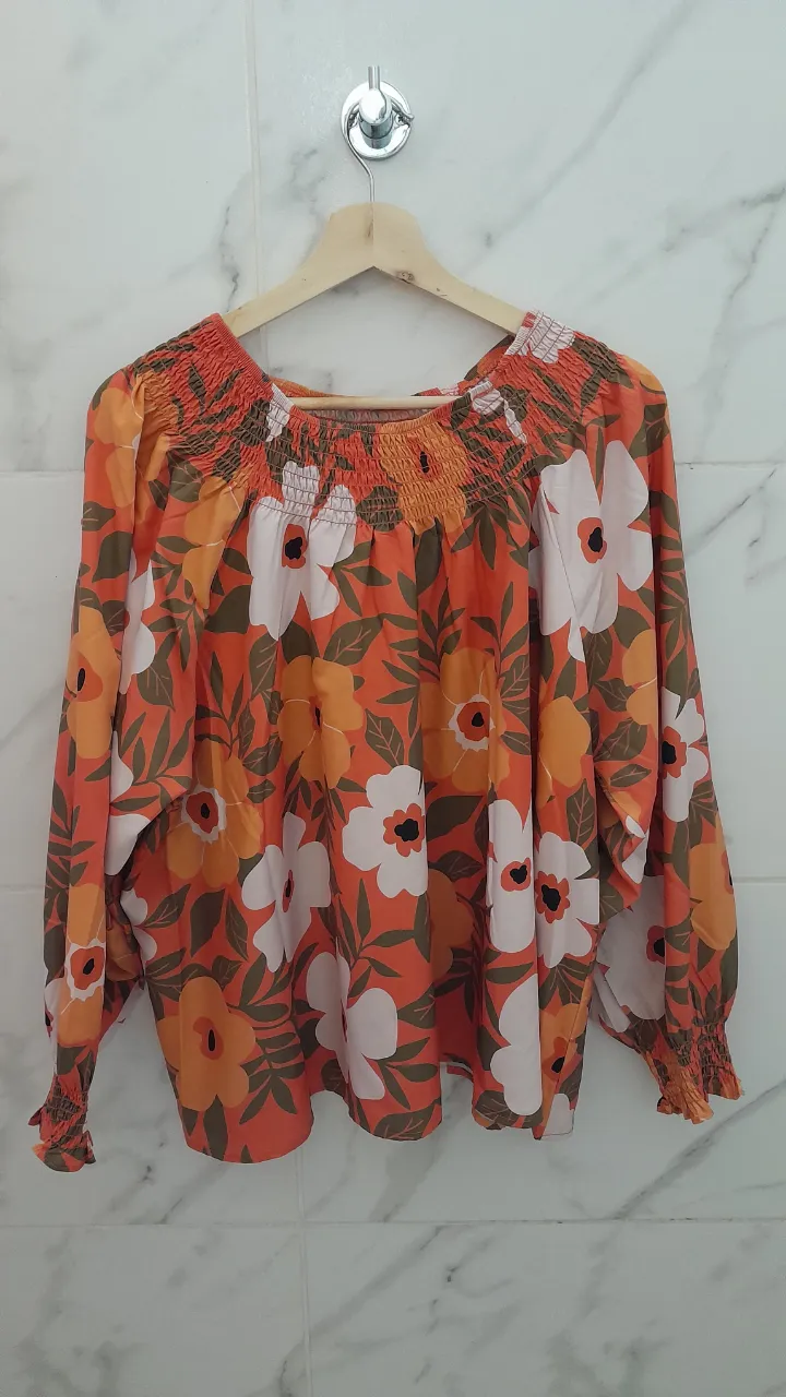 Blusa súper linda y cómoda con estampa floral vibrante en tonos naranjas y blancos. Tiene mangas largas con puños elastizados y un escote con fruncido que le da un toque canchero. Ideal para un look relajado y con onda.