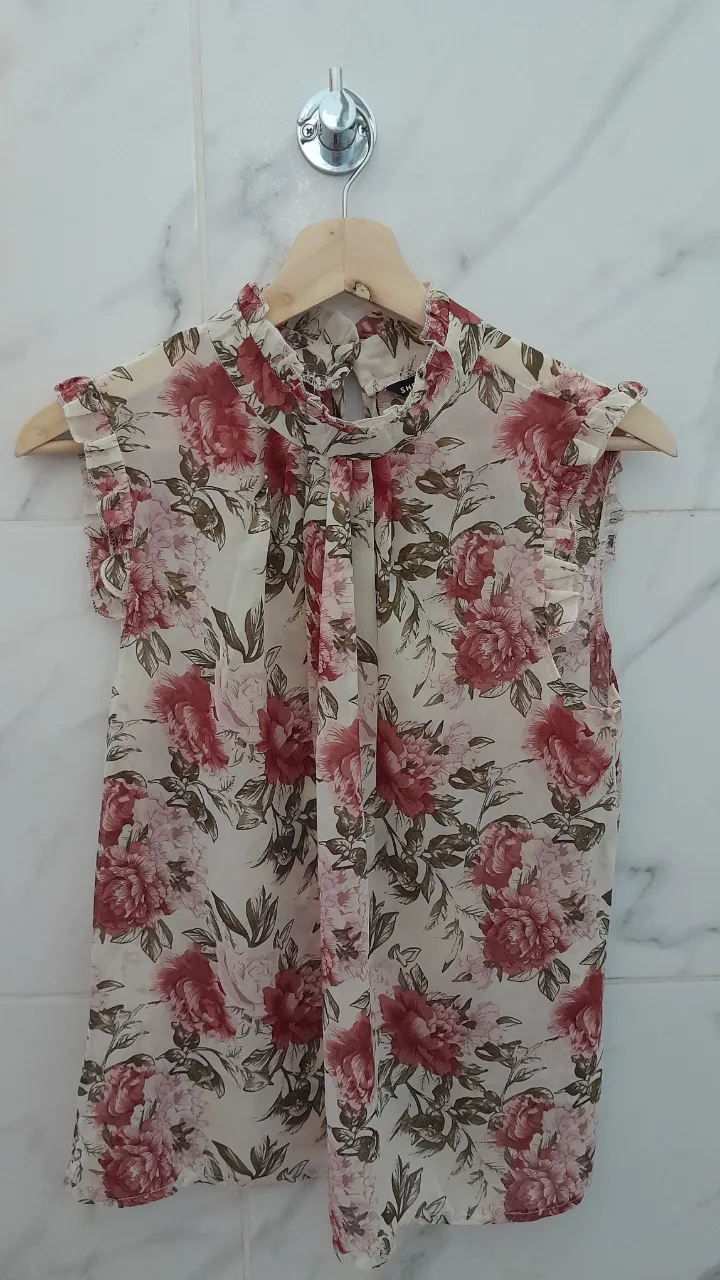 Blusa de gasa con estampado floral súper delicado y romántico. Posee cuello alto con detalle de volados y mangas cortas con terminación de volados. Ideal para un look elegante y femenino.