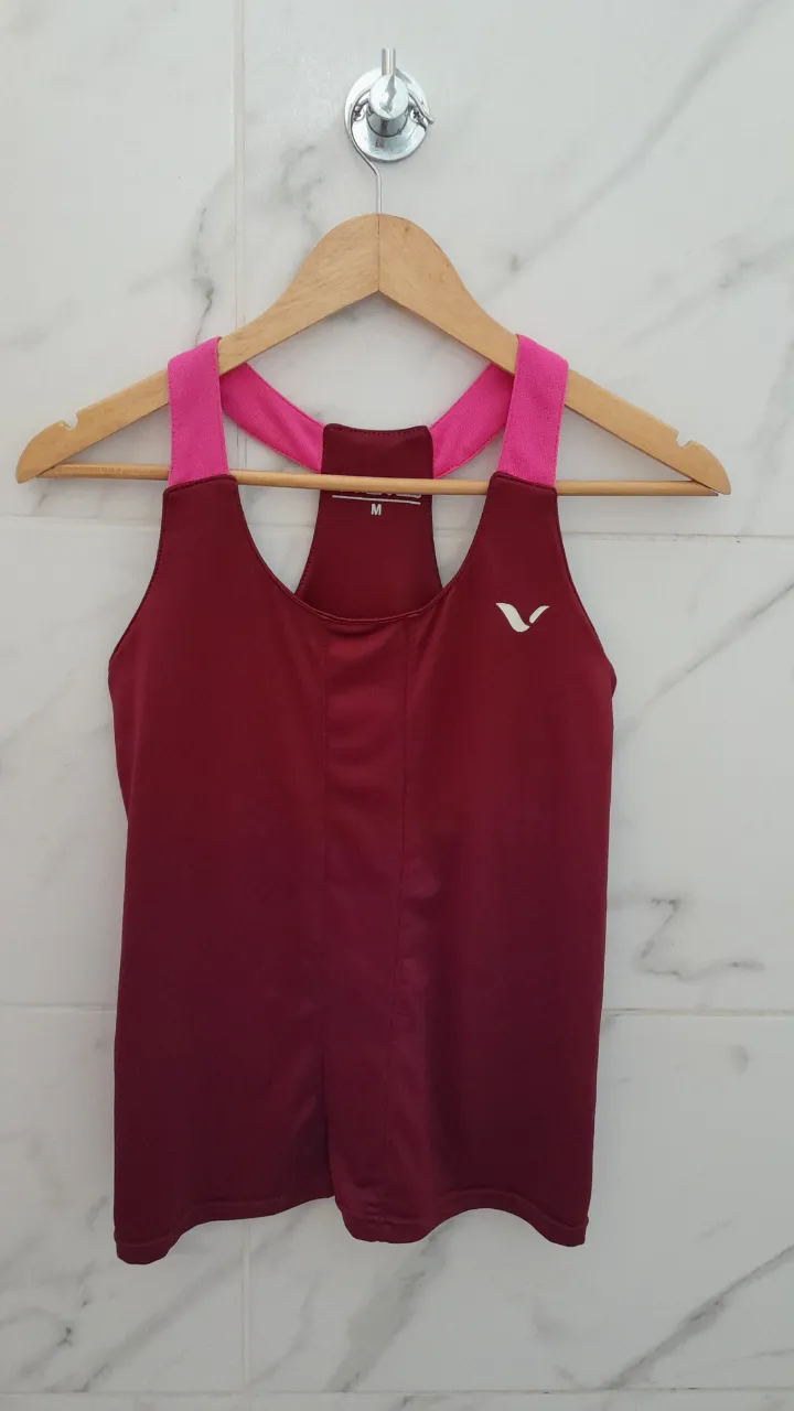 Musculosa deportiva color bordó con tiras rosas. Posee logo blanco en el frente y detalles reflectantes en la espalda.