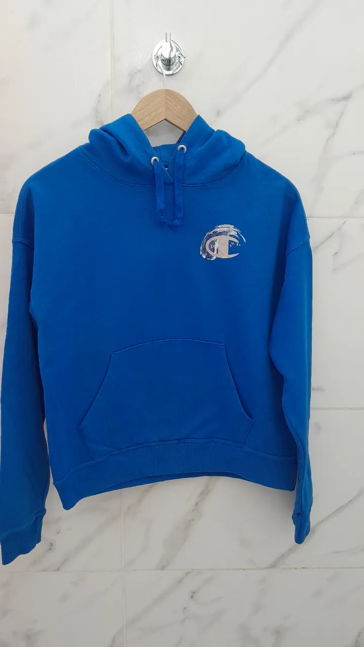 Buzo azul con capucha y cordones. Posee bolsillo canguro al frente y un logo estampado en el pecho.