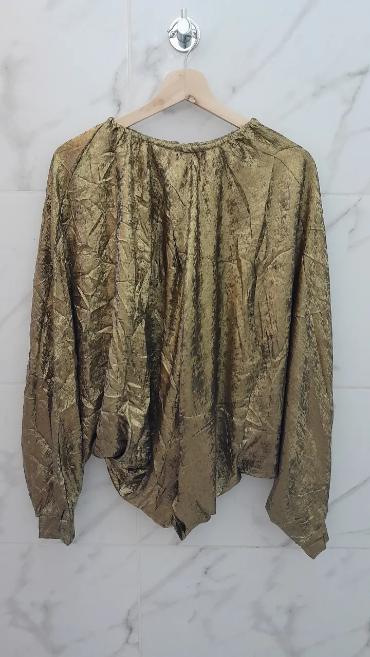 Blusa abierta de ambos lados dorada con textura arrugada y mangas largas. Diseño moderno y llamativo, ideal para un look de noche o fiesta.