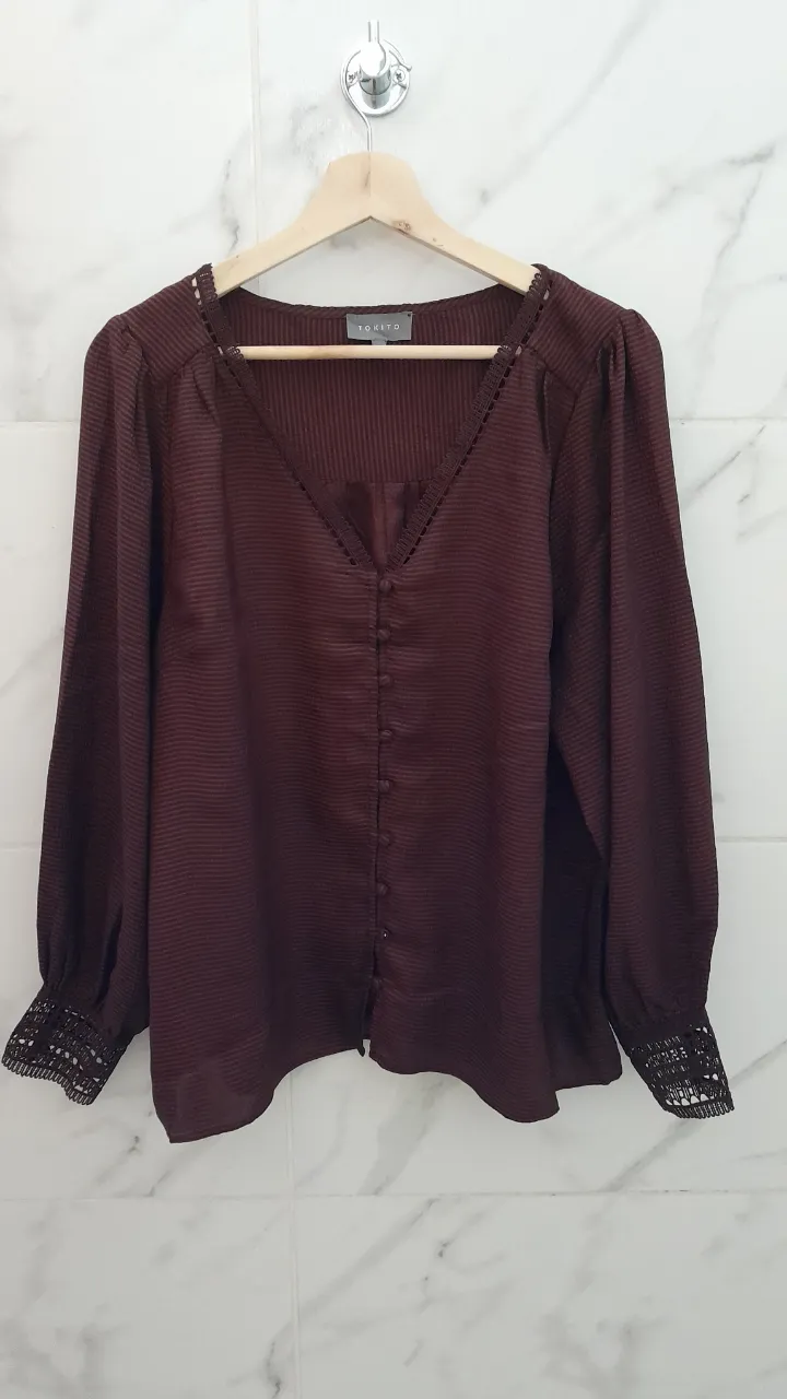 Blusa de manga larga en color bordo , con detalles de encaje en los puños y escote en V con botones. Un diseño elegante y femenino, perfecto para ocasiones especiales o para darle un toque sofisticado a tu look diario.