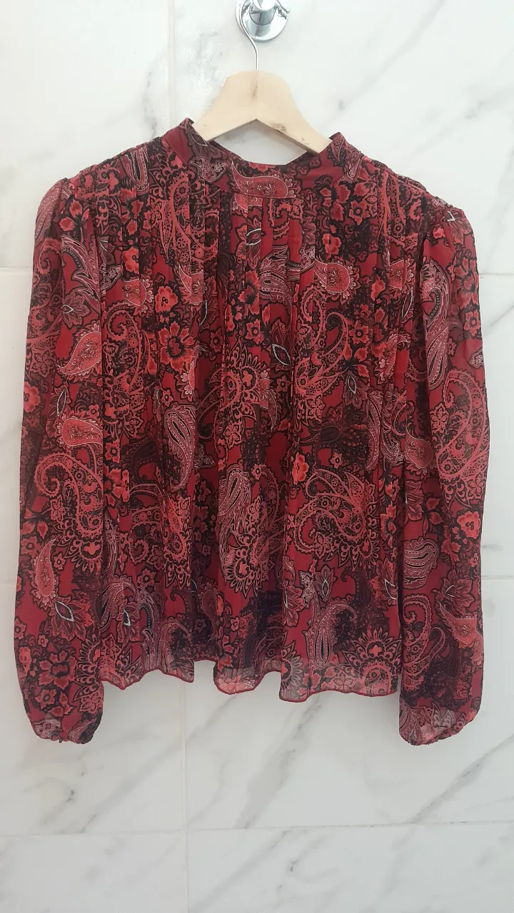 Blusa estampada con cuello alto y mangas largas. Diseño paisley en tonos rojos y negros, ideal para un look canchero y con onda.