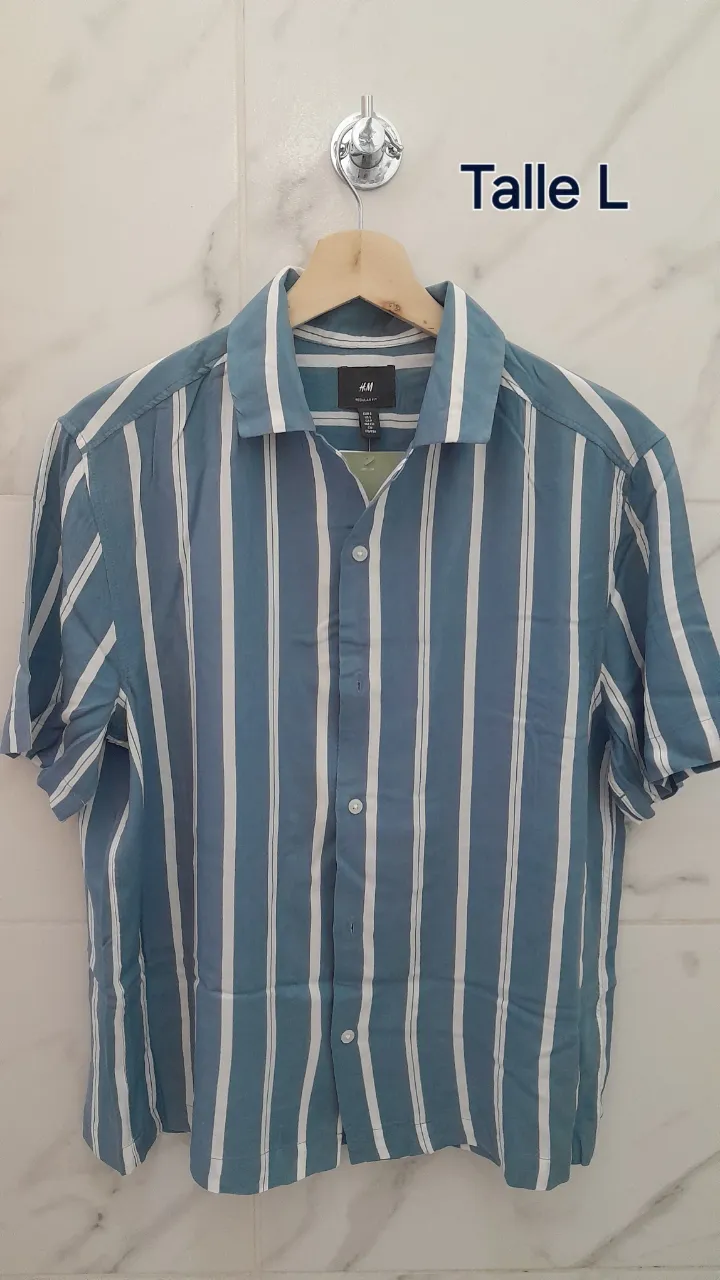 Camisa a rayas verticales celestes y blancas, con cuello y botones al frente. Manga corta.