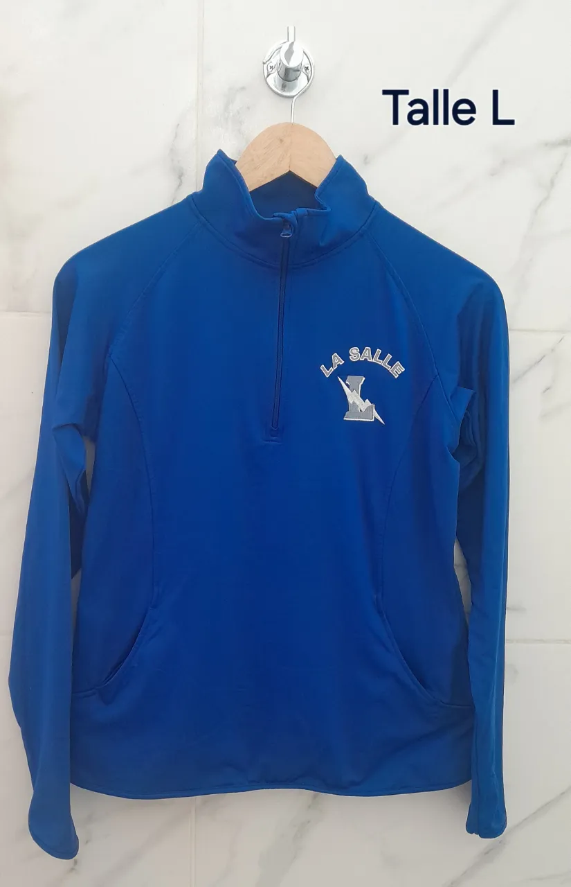 Buzo deportiva azul con cuello alto y cierre hasta la mitad del torso. Posee un bolsillo canguro en la parte delantera y puños con ojal para el pulgar.