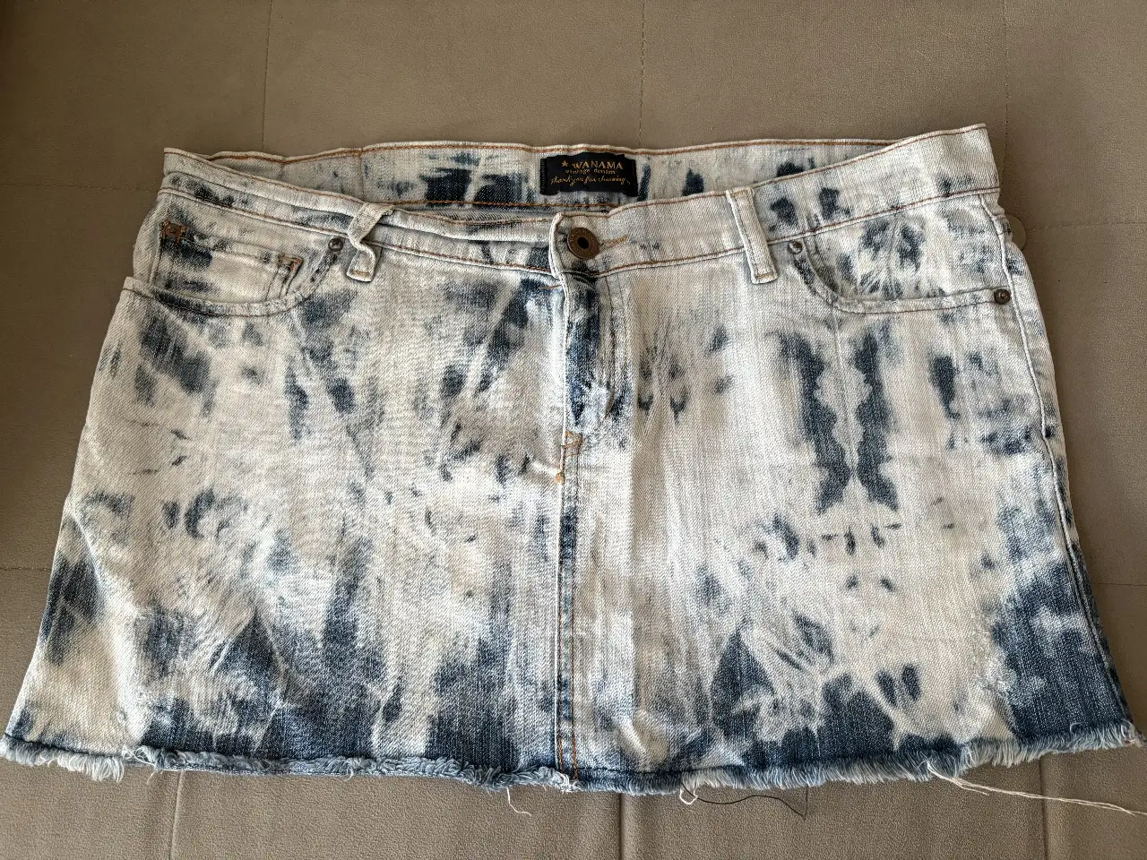Mini de jean Wanama efecto batik en blanco y azul. Talle M tiro bajo. Corte clásico con detalles de desgaste en el borde inferior.