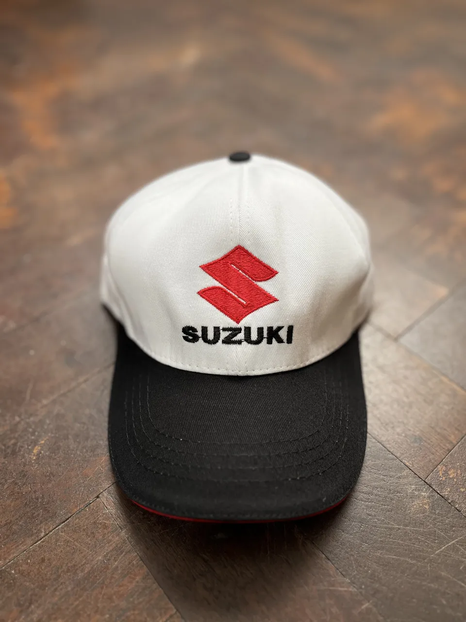 Gorra blanca y negra con el logo de Suzuki bordado en rojo y negro. 