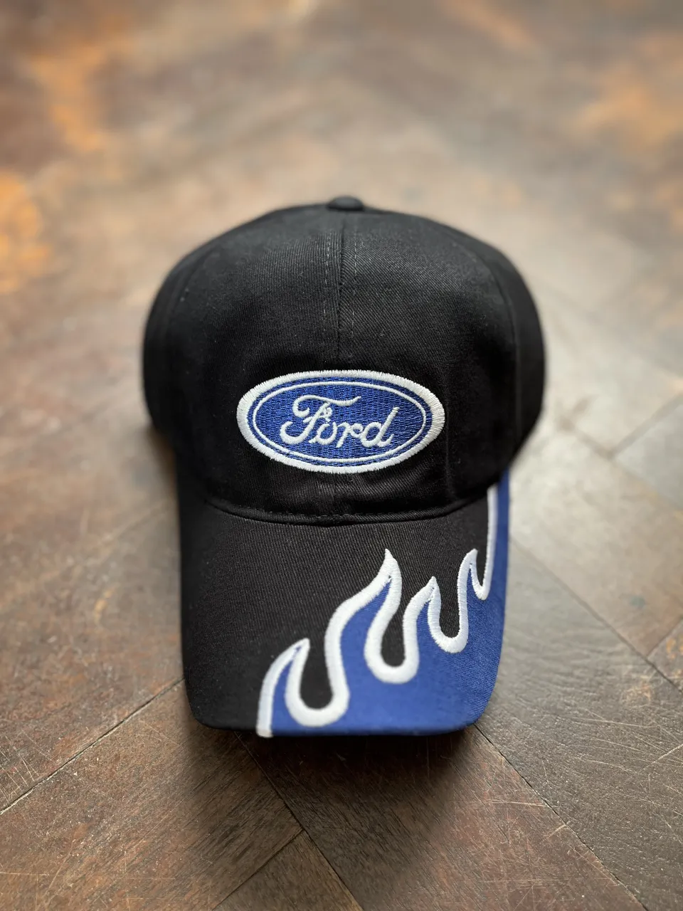 Gorra negra con logo de Ford bordado en blanco y azul. Detalle de llamas azules y blancas en la visera. ¡Un accesorio con onda para los fanáticos de Ford!