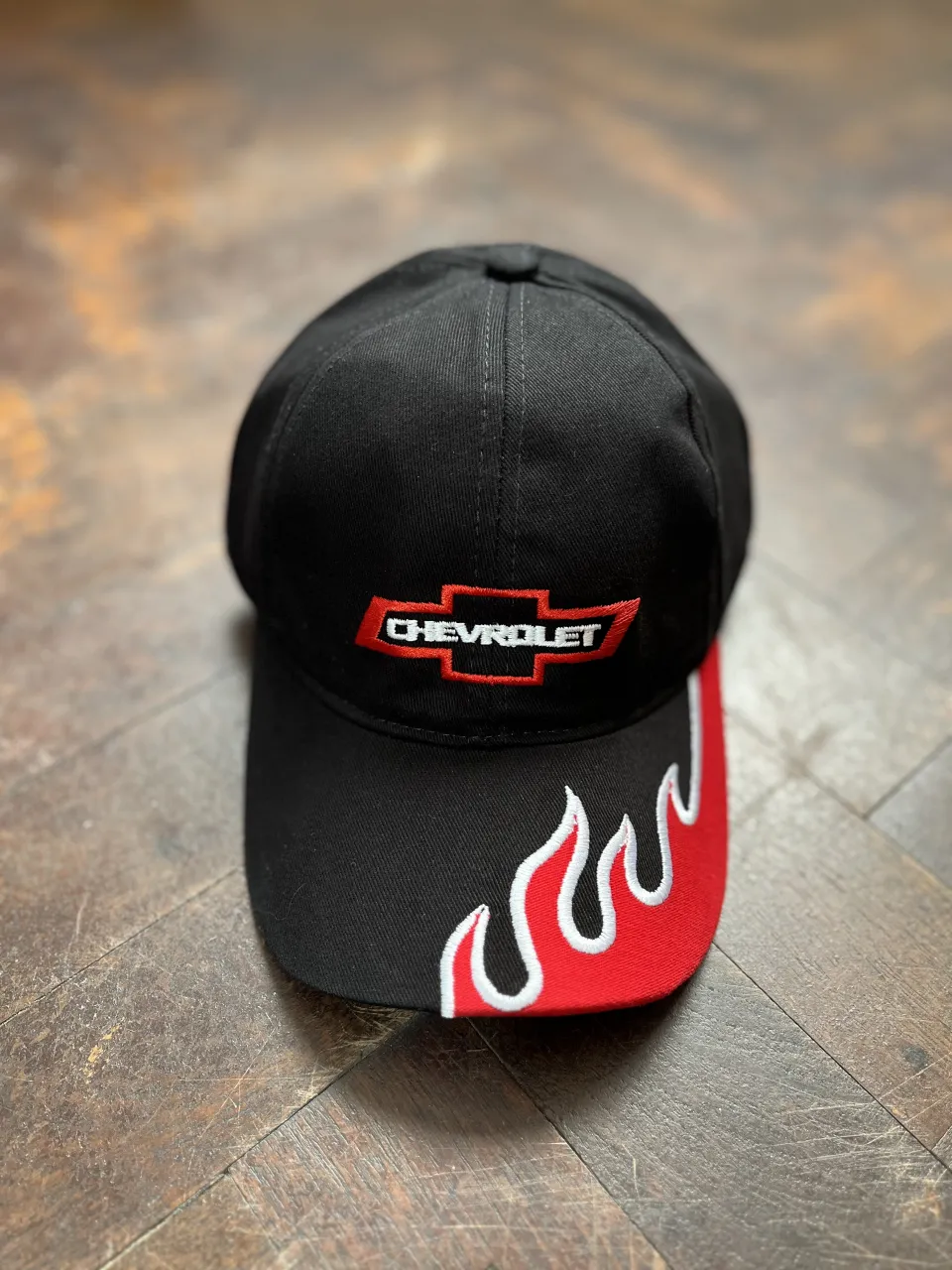Gorra negra con logo de Chevrolet bordado en rojo y blanco. Detalle de llamas rojas y blancas en la visera. "Find New Roads" bordado en la parte trasera.