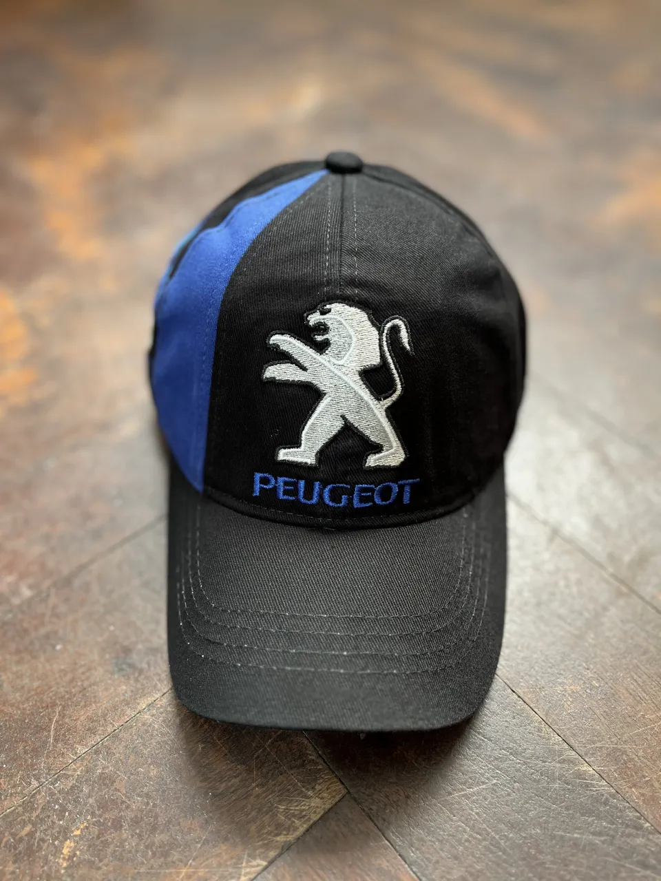 Gorra negra con detalles en azul y el logo de Peugeot bordado en blanco y plateado. Ideal para los fanáticos de la marca o para un look casual y deportivo.