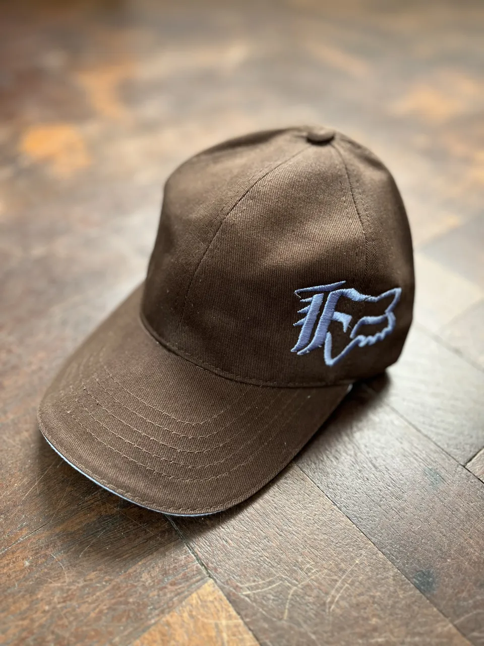 Gorra marrón con bordado y detalles en celeste. 