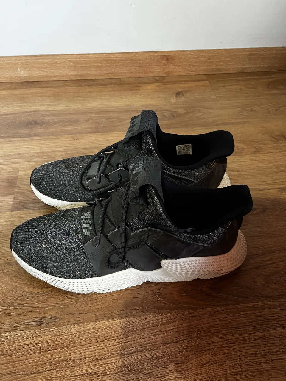 Zapatillas deportivas Adidas, ideales para running o entrenamiento. Diseño moderno en negro con detalles en blanco y dorado. Perfectas para un look urbano y activo.